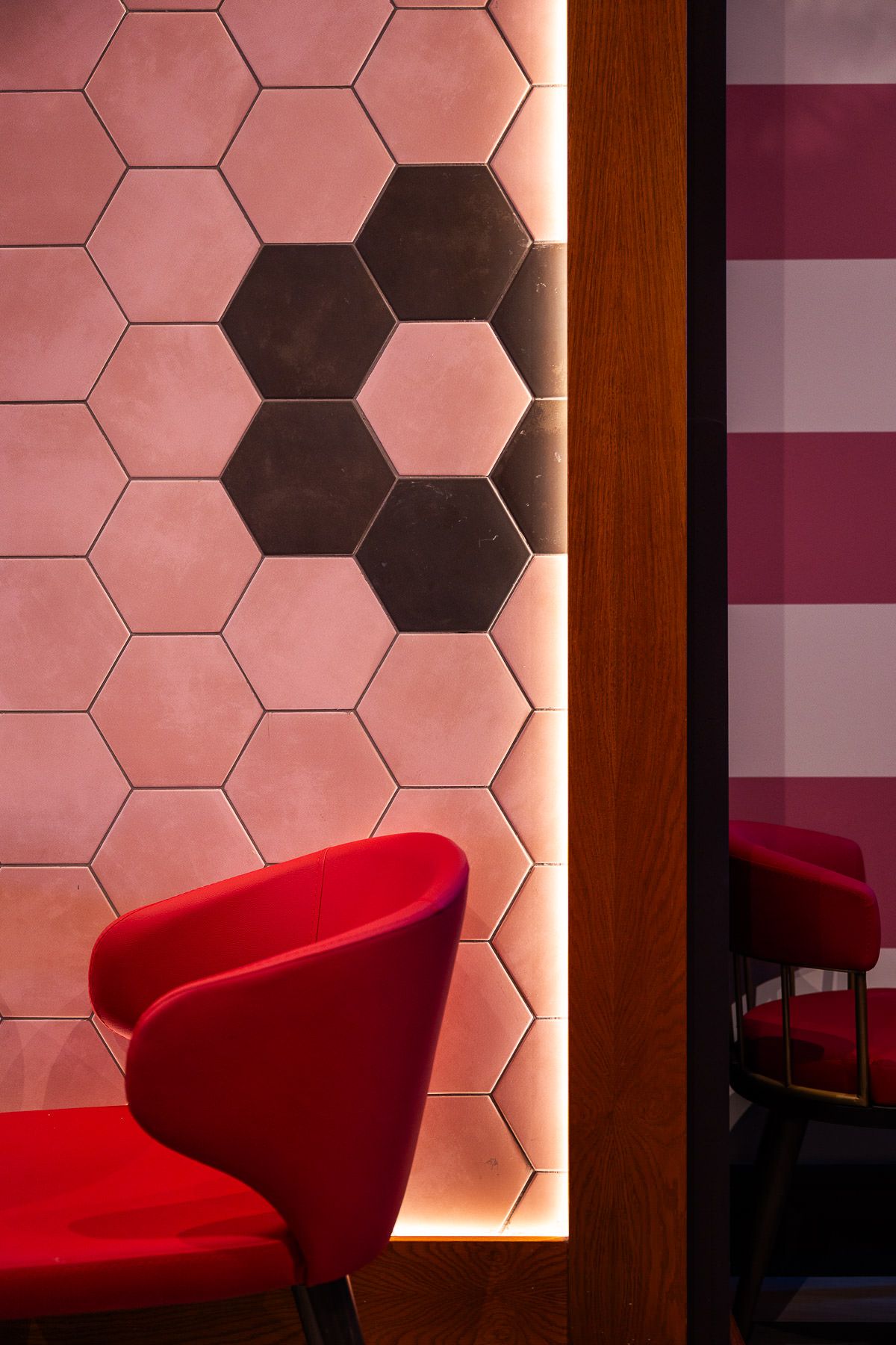 Close-up of modern interior with pink and black hexagonal tiles, warm lighting, and a vibrant red chair.