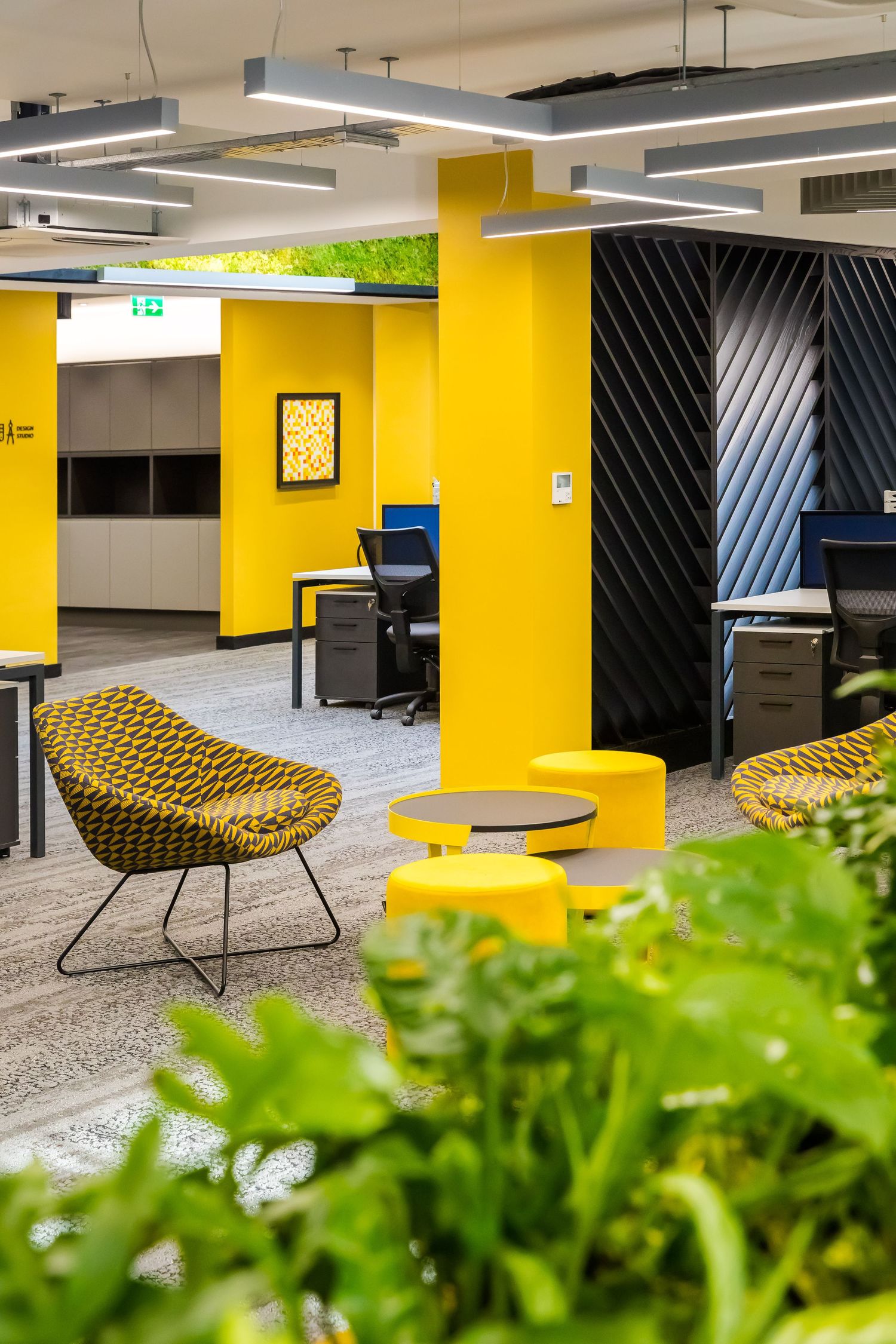 Bright, modern office space featuring bold yellow accents, geometric seating, and integrated greenery for a vibrant, contemporary workspace.