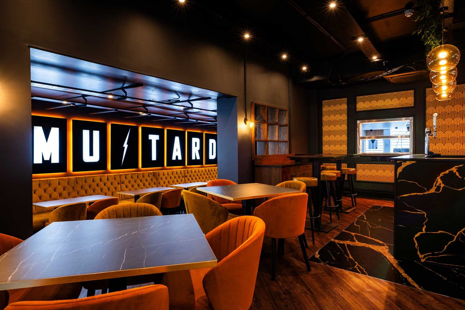 Stylish restaurant interior in Durham with warm lighting, velvet seating, marble tables, and a glowing “Mustard” feature wall and bar area.