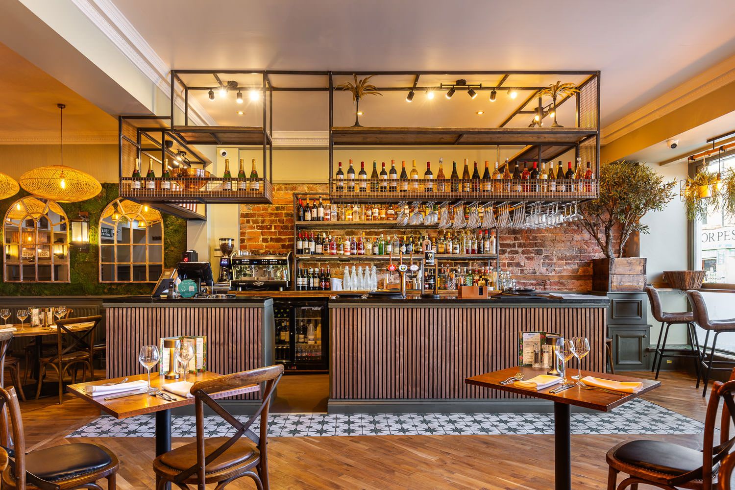 Warm, inviting bar with rustic brick walls, wooden accents, hanging wine glasses, and greenery enhancing the cozy ambiance.