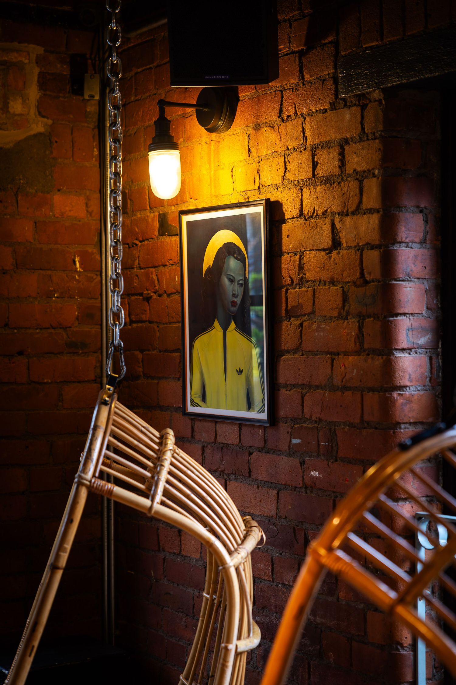 Warm industrial interior with exposed brick, rattan seating, and a framed portrait illuminated by soft, ambient lighting.