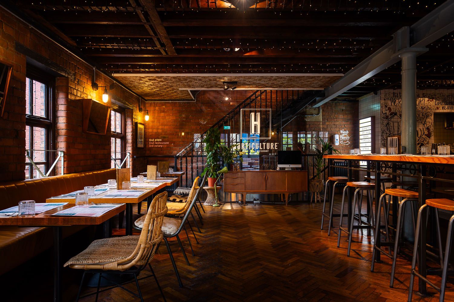 Industrial-style dining space with exposed brick walls, wooden furniture, warm lighting, and greenery creating a cozy yet modern vibe.