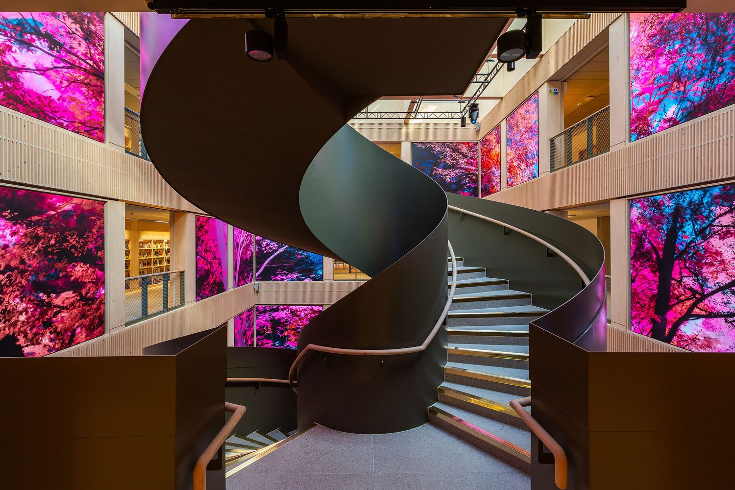 Contemporary curved staircase with illuminated steps and vibrant digital artwork displays in a modern cultural centre interior.