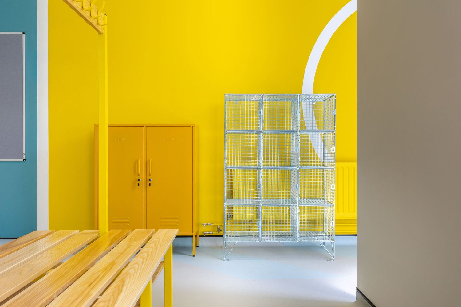 Bright modern locker room interior with bold yellow walls, wooden benches, and metal storage units in a clean contemporary design.