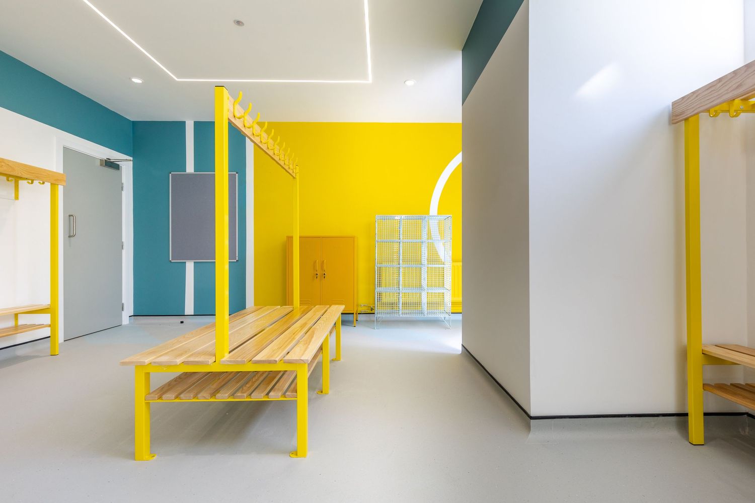 Bright and modern locker room with bold yellow accents, teal walls, and minimalist wooden benches.
