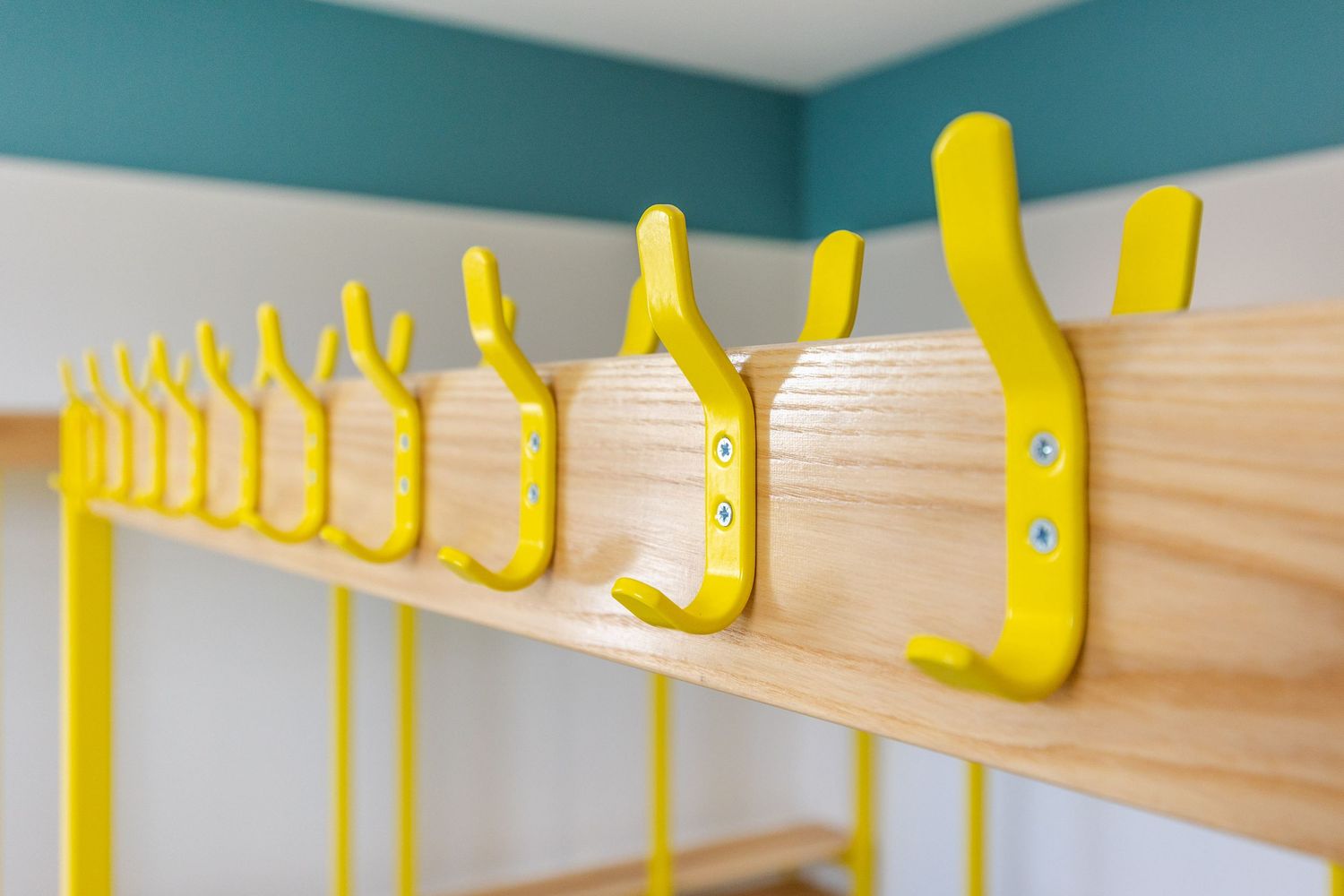 Close-up of bright yellow coat hooks on a wooden rail, showcasing clean, modern school interior design with bold, playful colour accents.