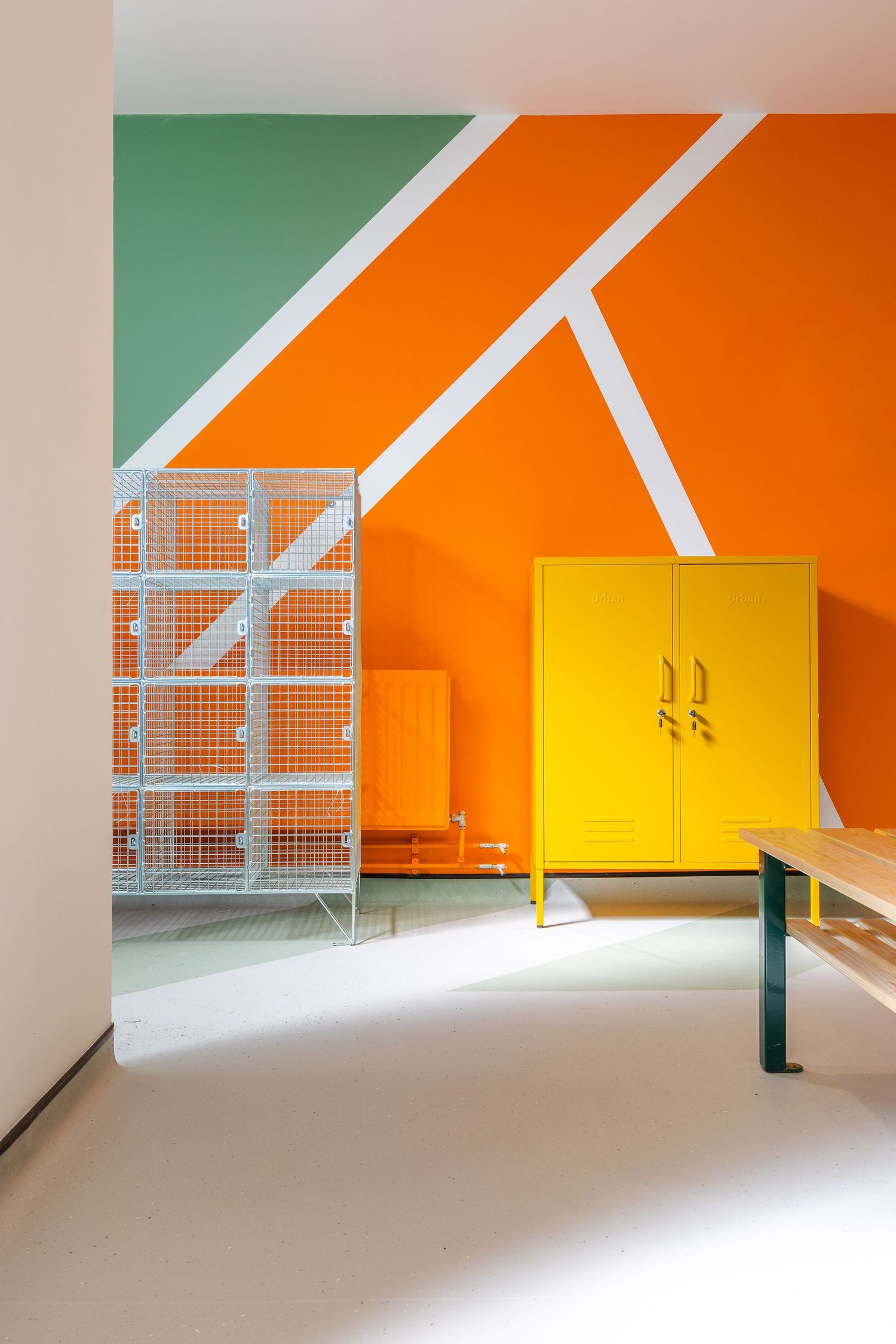 Vibrant locker room with bold orange, green, and yellow accents and geometric wall design for a playful modern look.