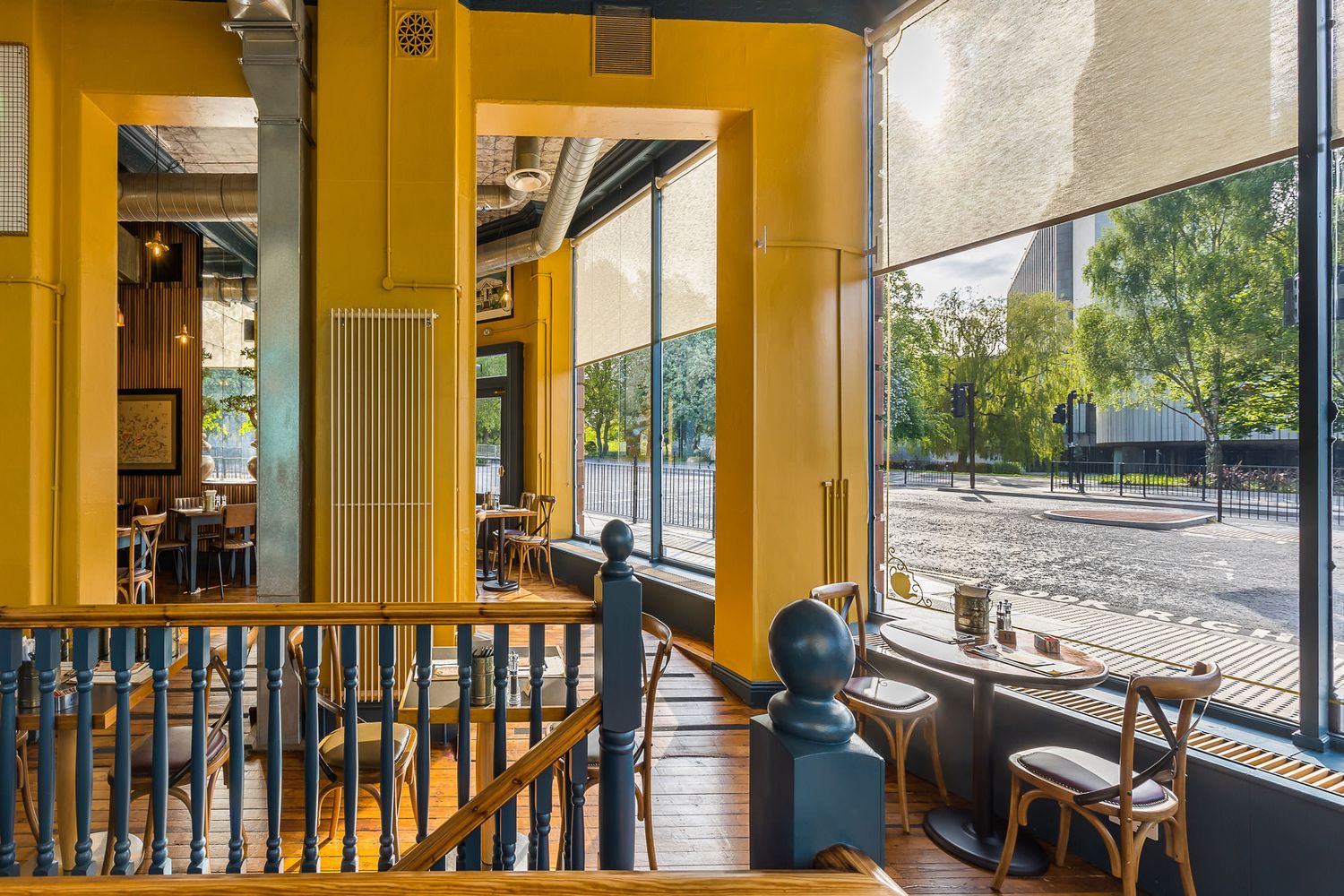 Bright tea house with yellow walls, large windows, natural light, wooden floors, and a cozy seating area overlooking the street.