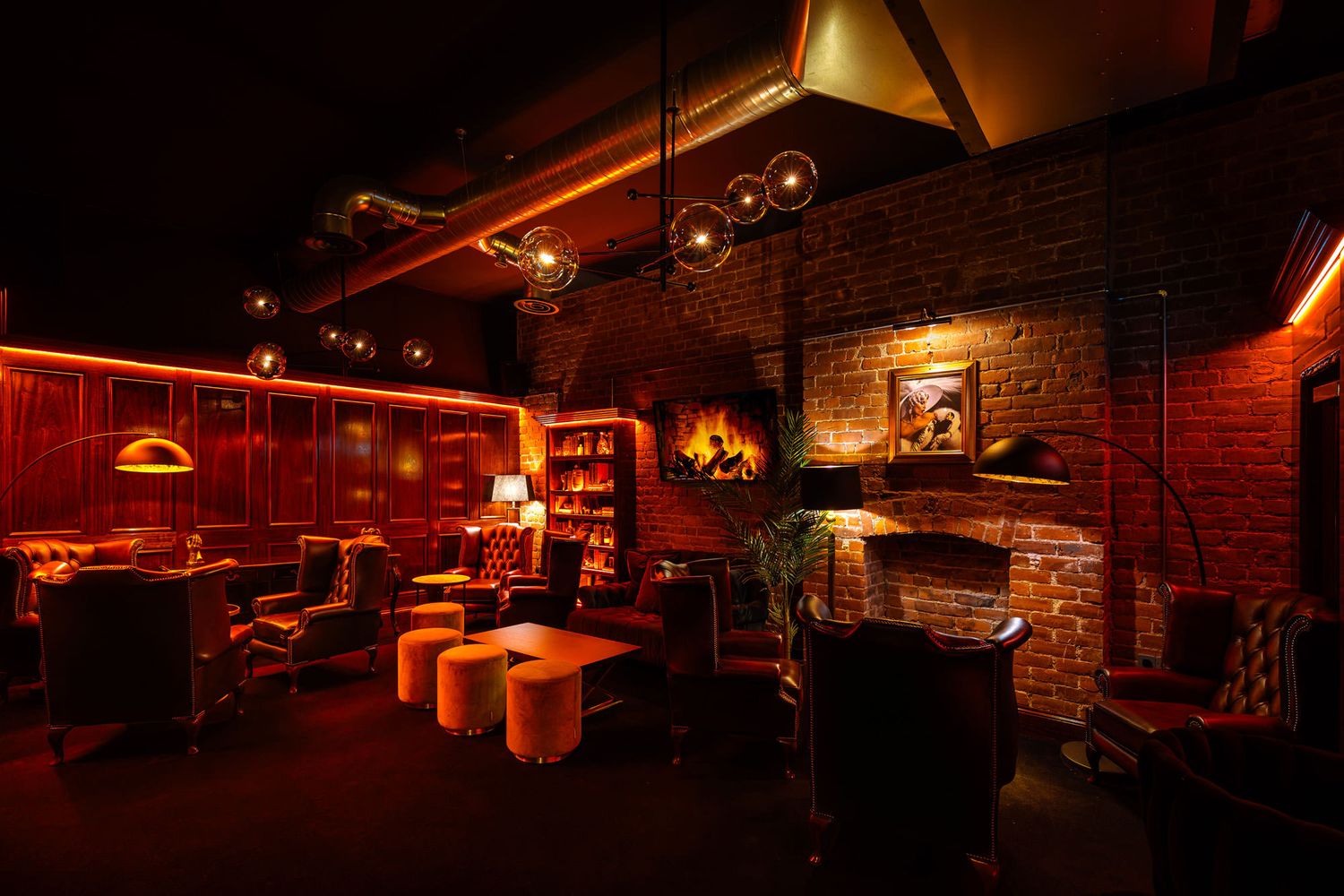 Cozy whiskey lounge with leather chairs, warm lighting, exposed brick walls, and a fireplace creating a sophisticated vintage ambiance.