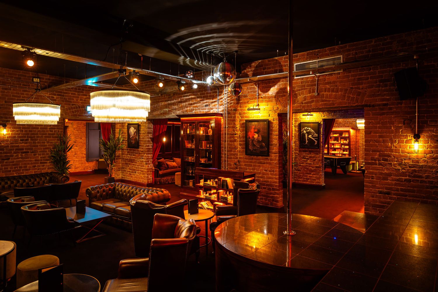 Cozy lounge with exposed brick walls, leather seating, warm lighting, chandeliers, vintage decor, and a sophisticated ambiance.