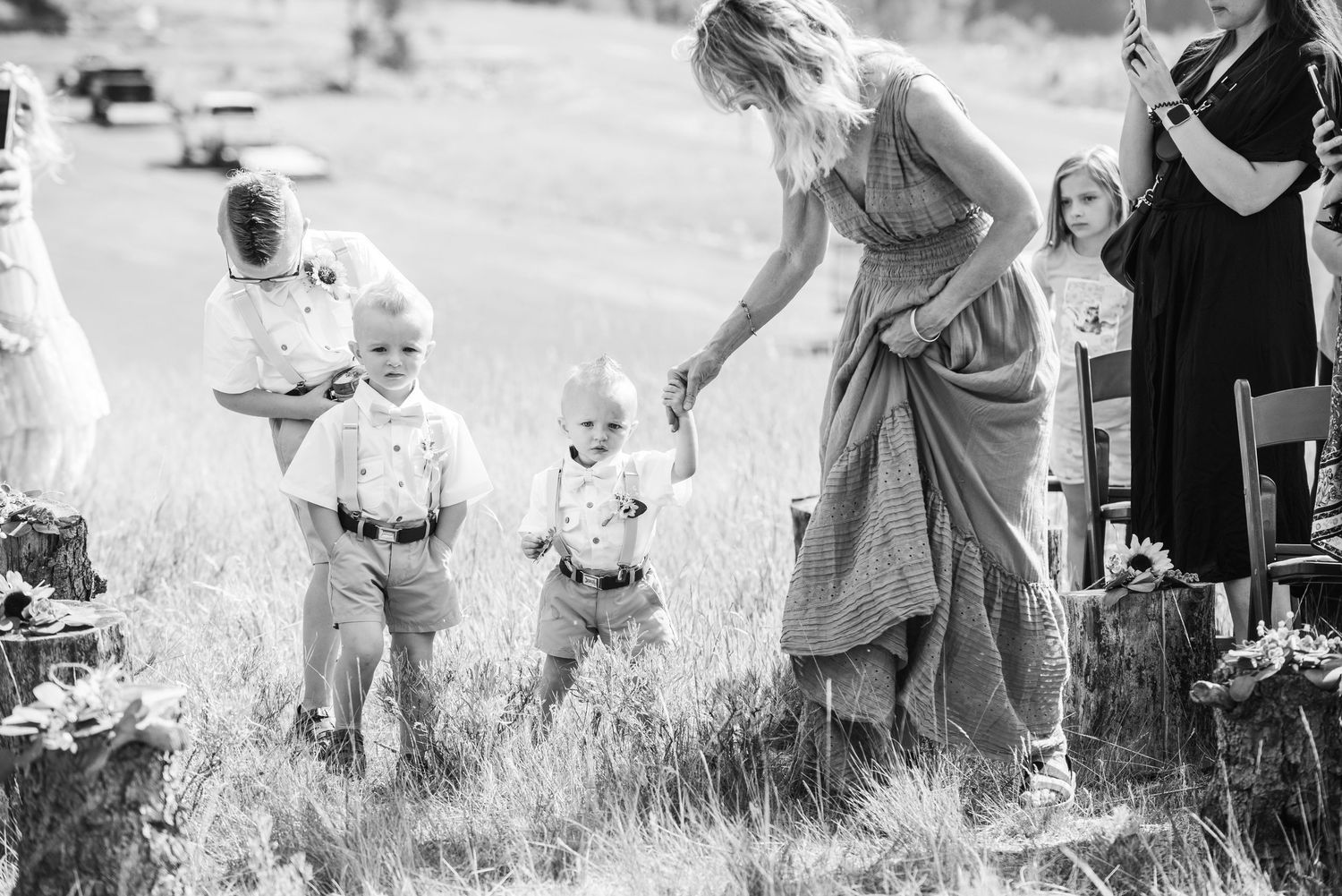 Black and white photo of children playing in a grassy field with an adult figure during a joyful outdoor moment.