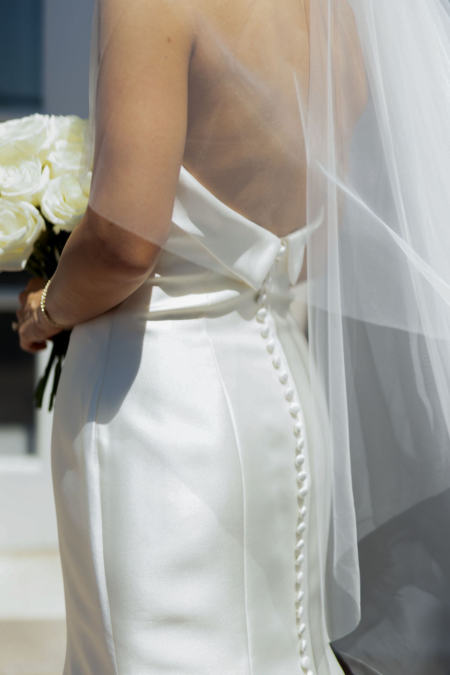 Close-up details of white wedding dress buttons and veil in elegant lighting.