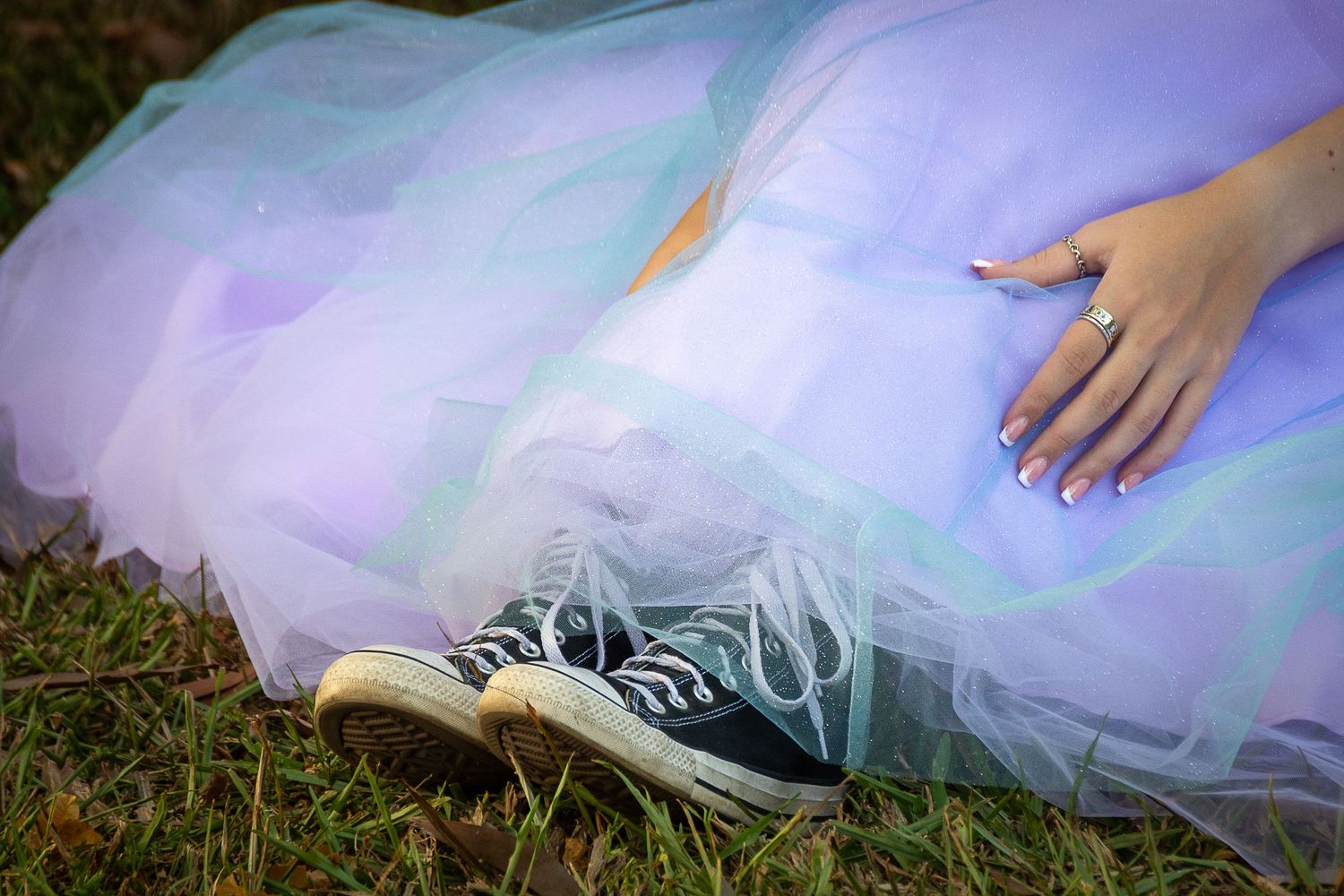 A hand rests on a pastel purple tulle skirt paired with a casual blue sneaker on grass.
