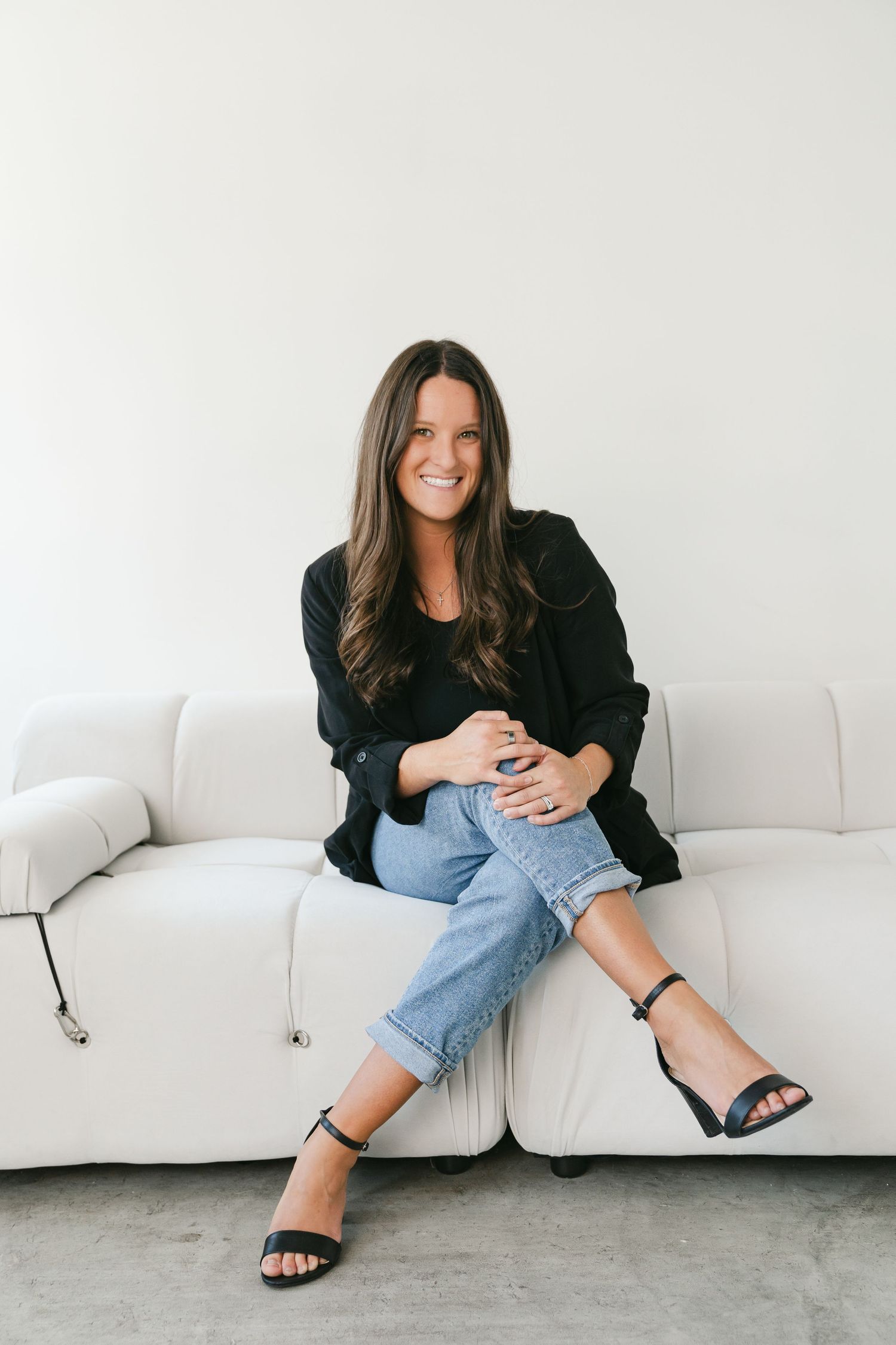 Casual lifestyle portrait of woman lounging on white couch in denim and black jacket.
