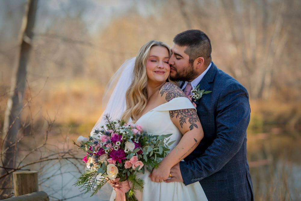 groom wearing a blue suit kissing bride's cheek while standing near a pond in the fall Boise wedding photographer