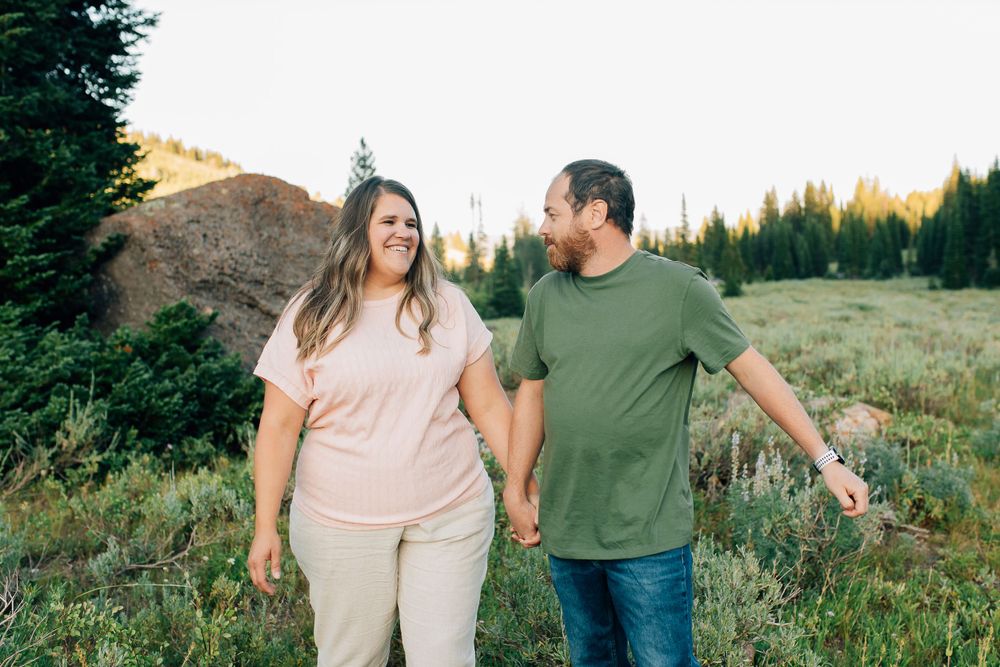 A couple walks together through a mountain meadow during golden hour.