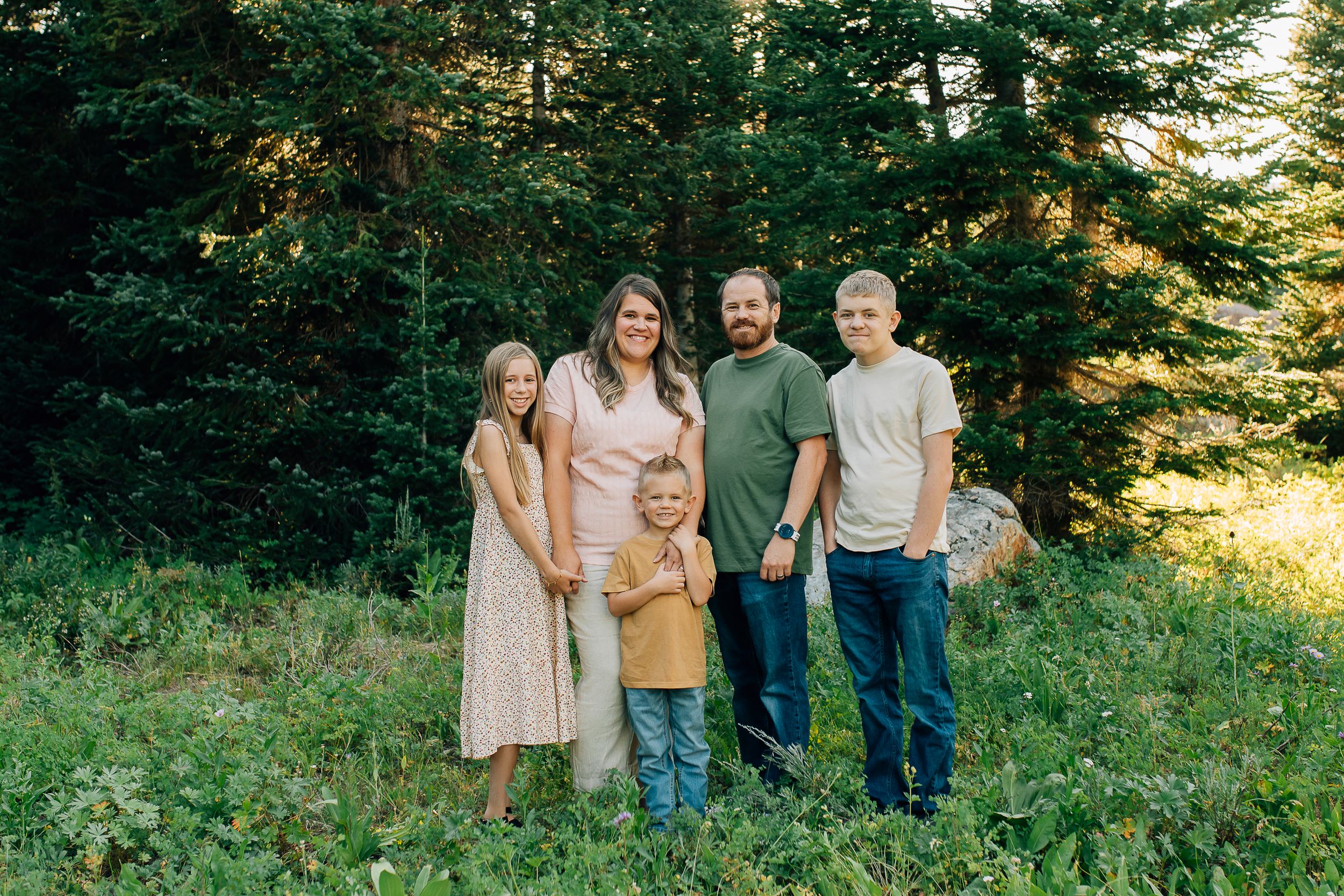 A family poses together outdoors in front of evergreen trees during a nature photo session.