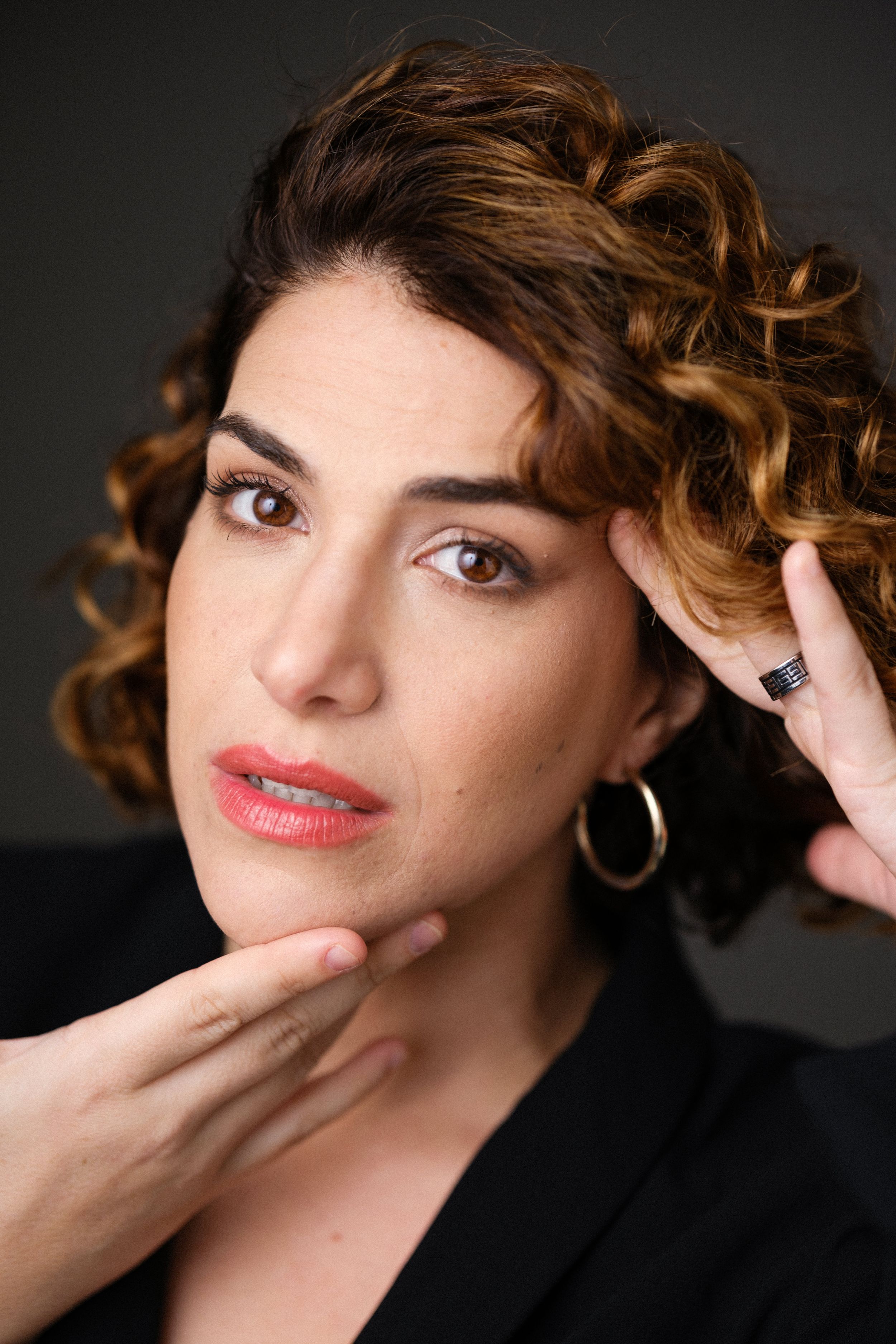 Close-up portrait with curly hair and black jacket showing contemplative pose.