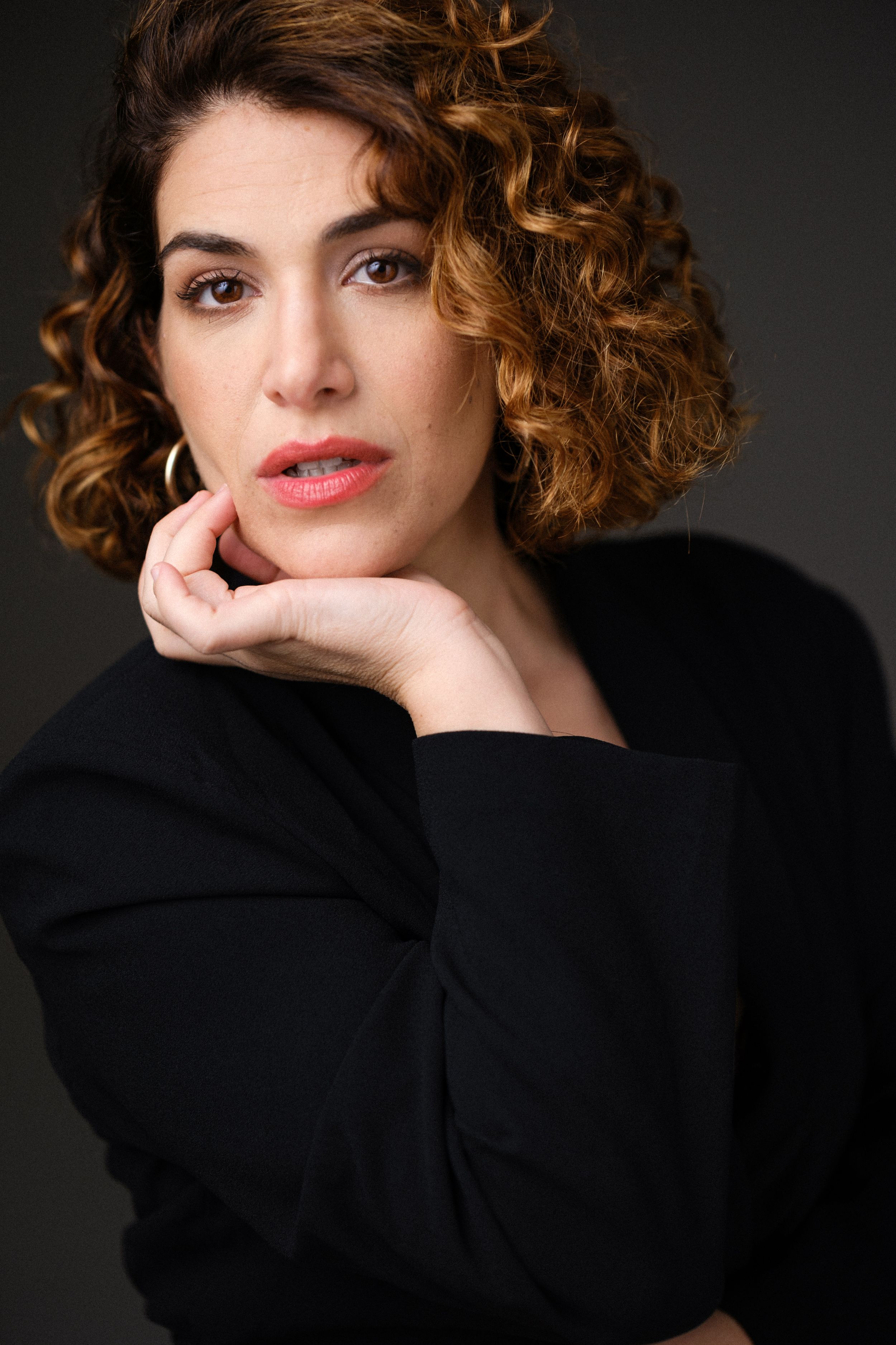 Artistic headshot with hand posed near face wearing black ensemble.
