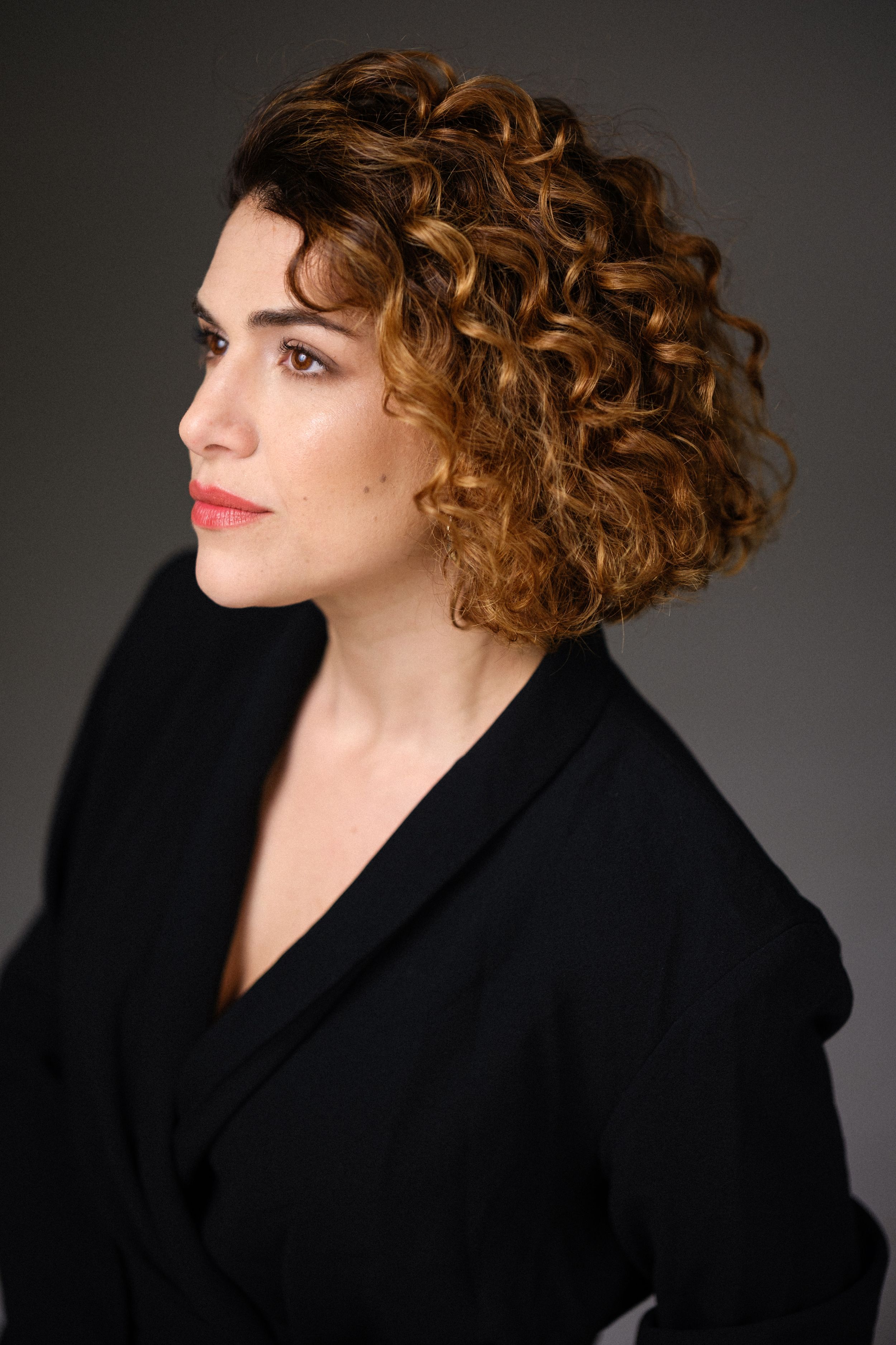 Side profile portrait in black blazer with styled curly hair.