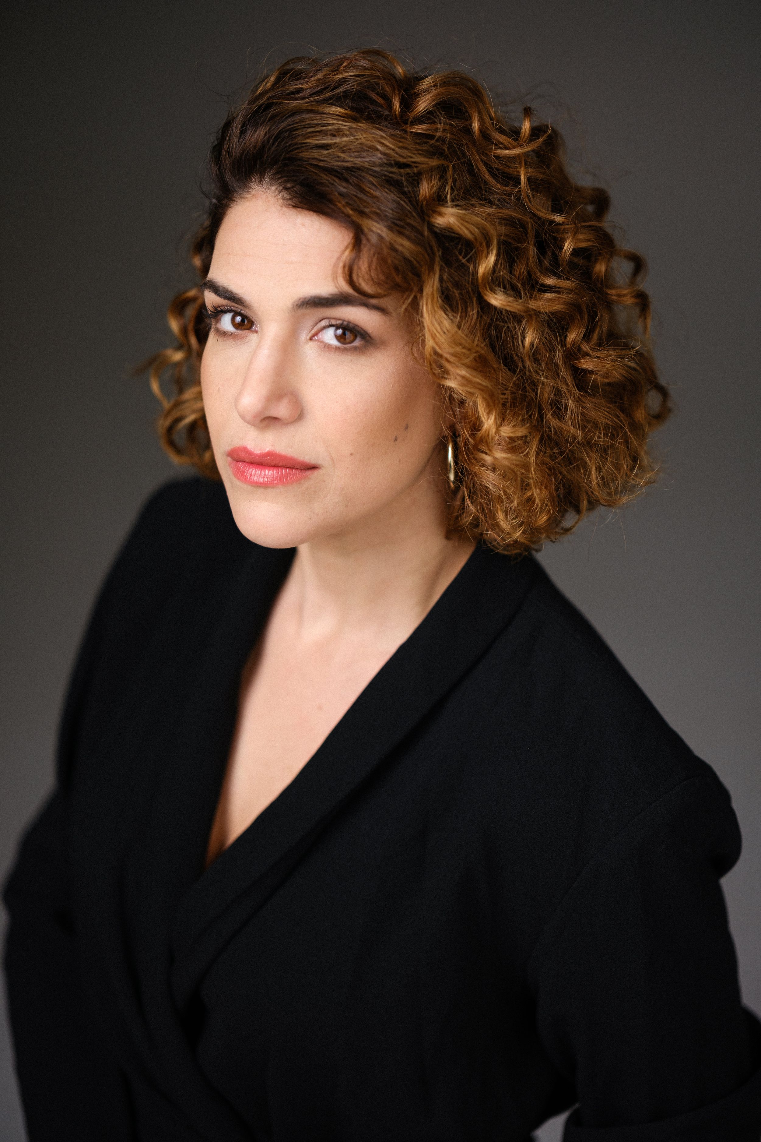 Professional studio shot in black coat with curled hair and bold makeup.