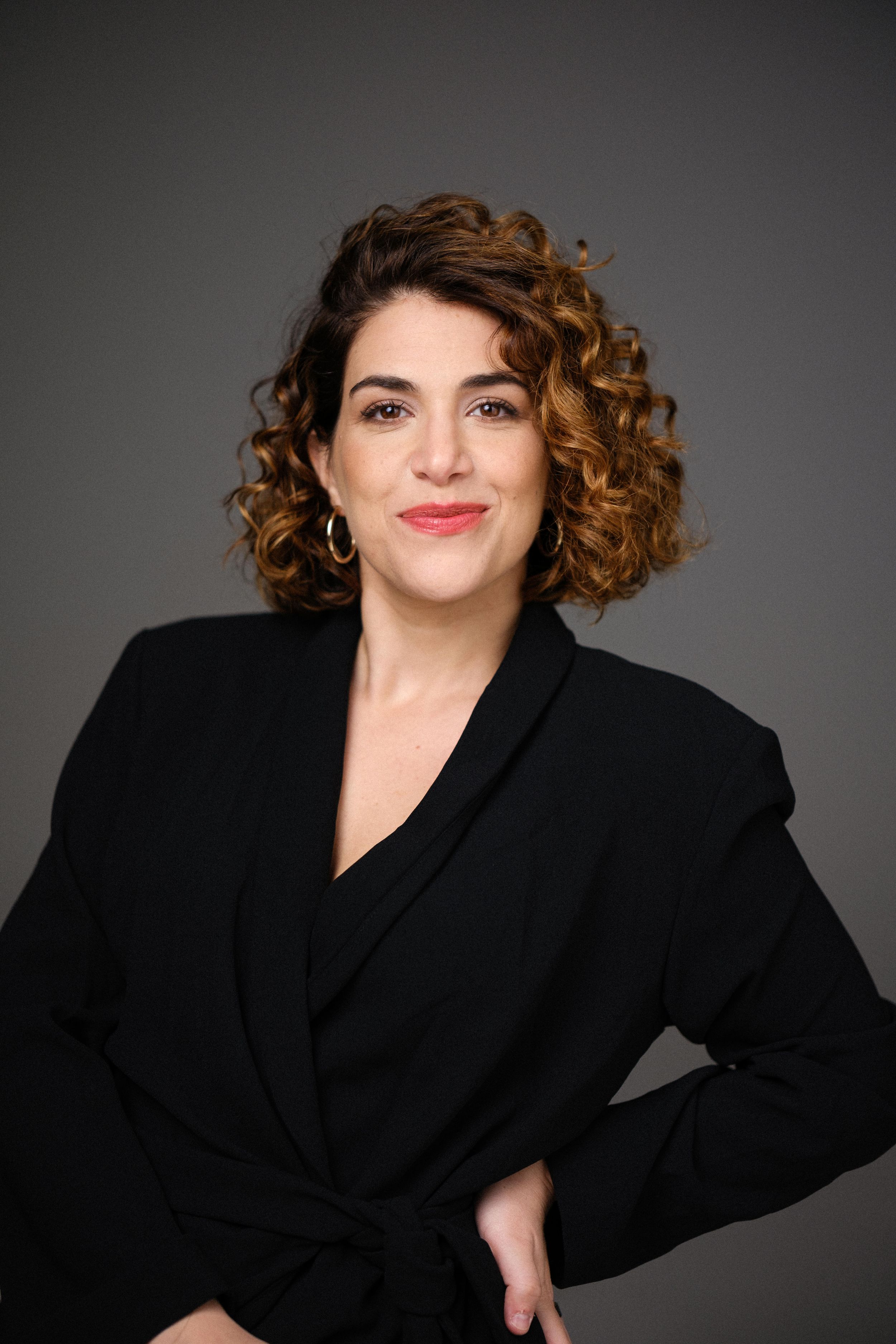 Artistic studio portrait in black attire with expressive pose against grey backdrop.