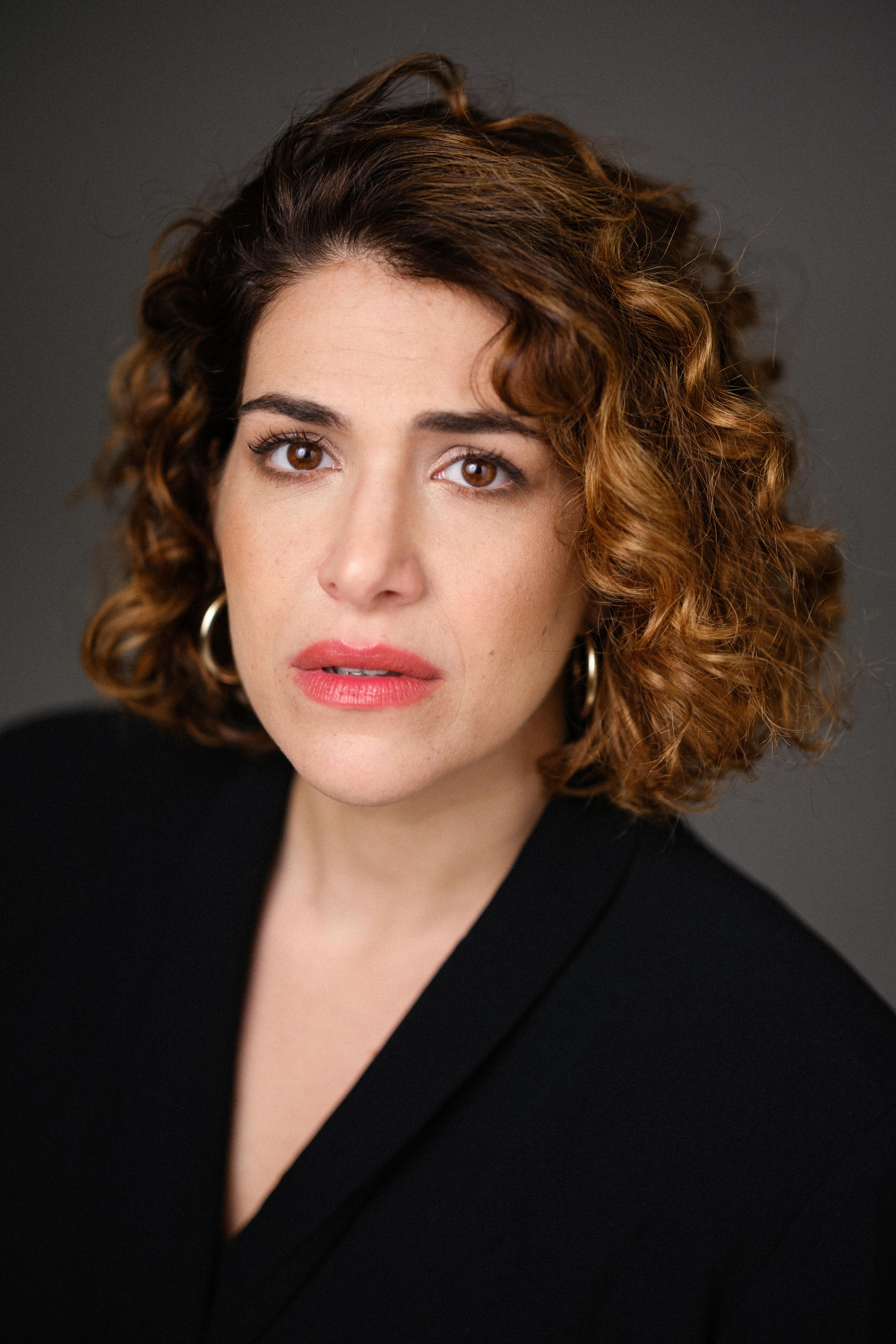 Close-up portrait with curly hair and bold lip color against dark backdrop.