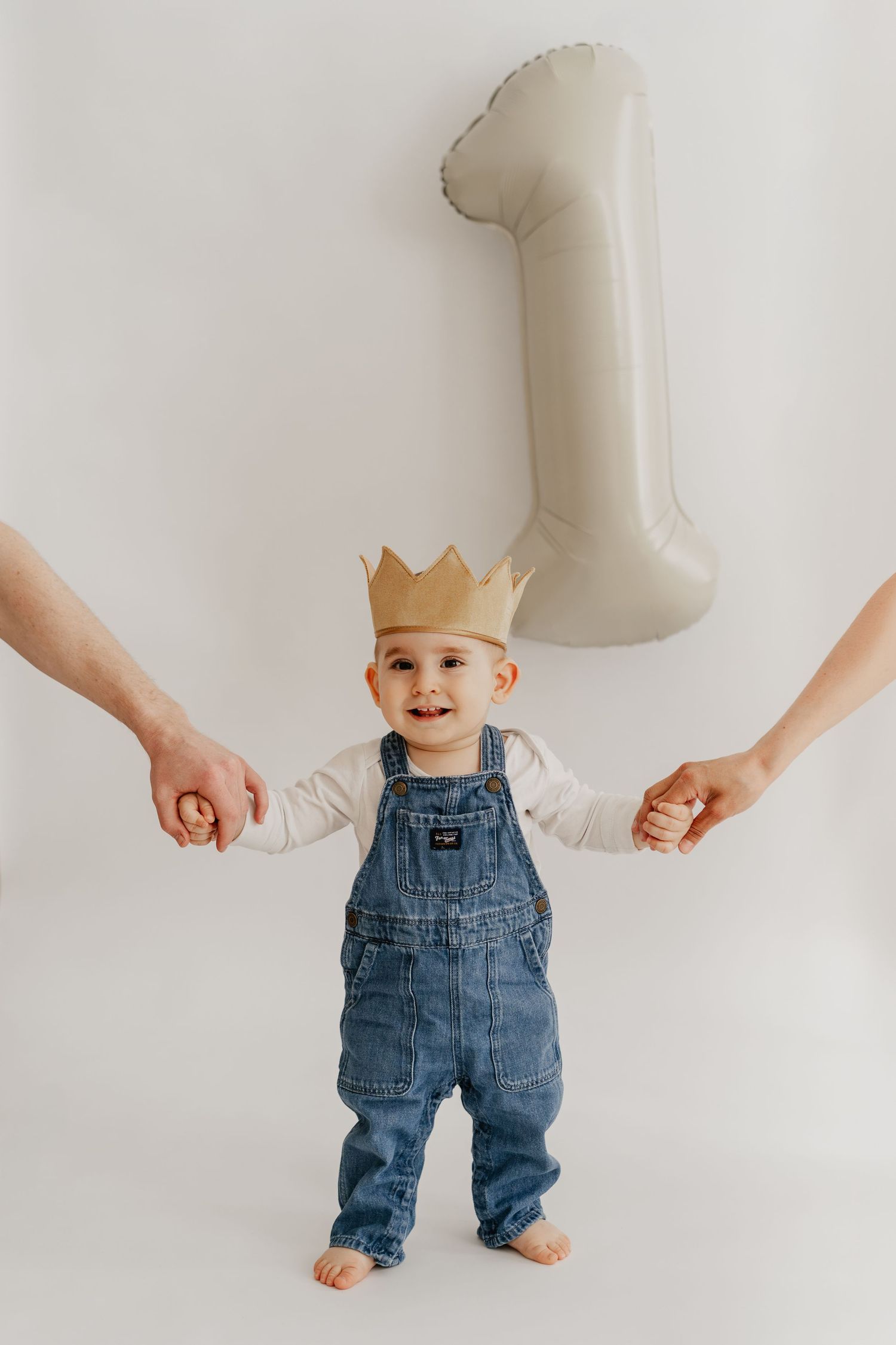 Babyshooting zum 1. Geburtstag im Fotostudio Stockerau. Bub steht mit Krone an den Händen der Eltern und lacht herzig