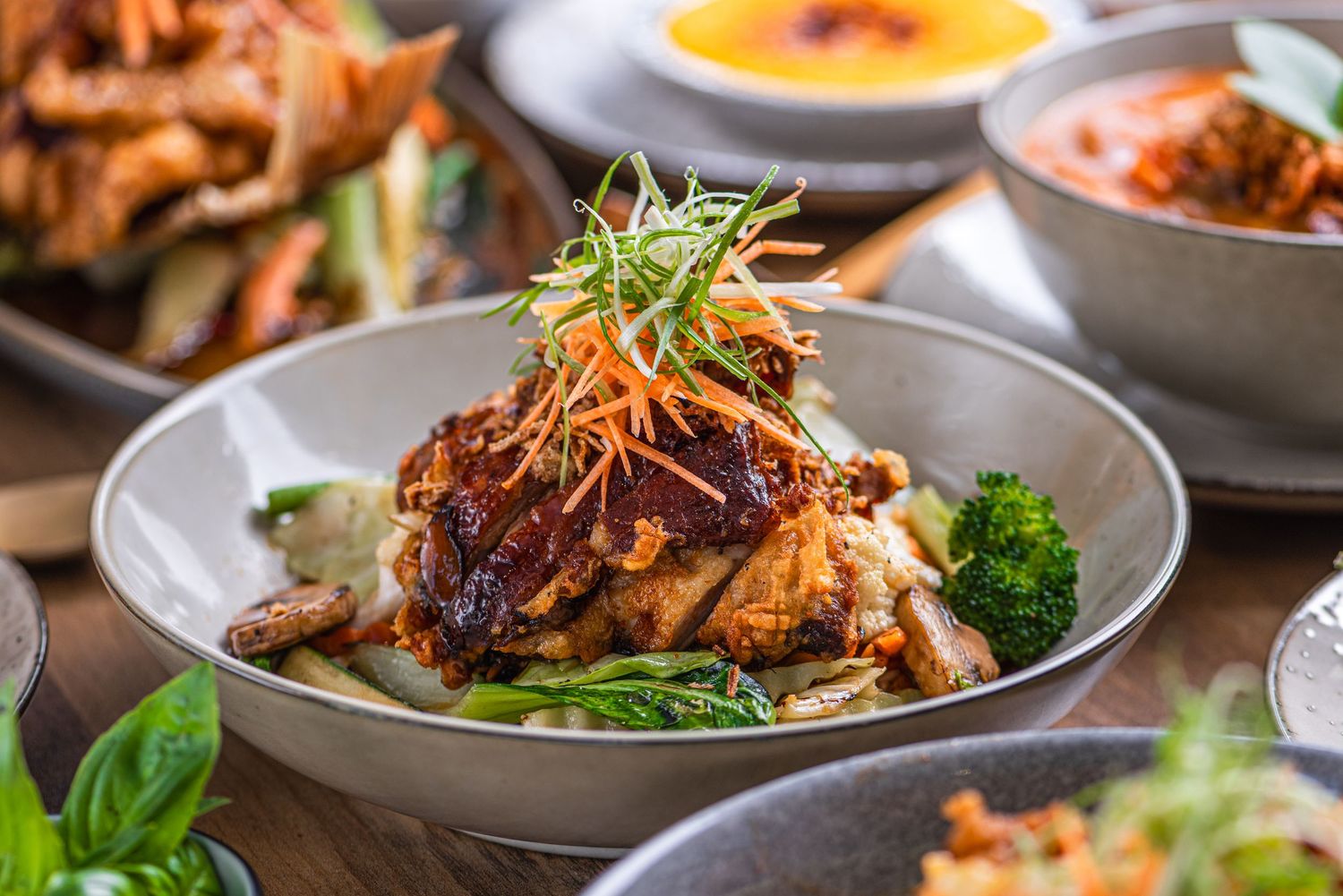 Rustic bowl of seared beef garnished with fresh basil leaves, surrounded by colorful Mediterranean dishes on a dark table.