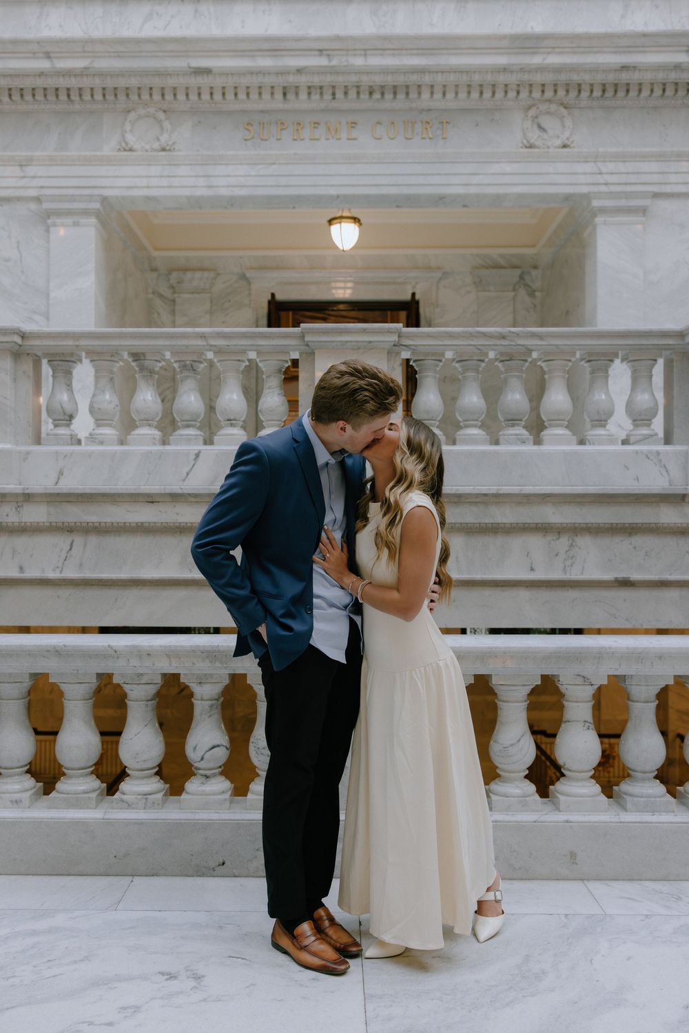 Couple sharing a kiss inside a marble Supreme Court building during their engagement photo session.