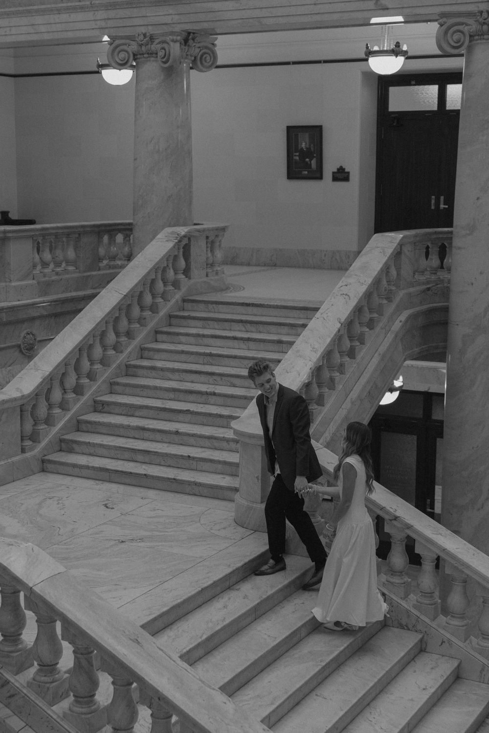 Bride and groom descend elegant marble staircase in grand historic building during wedding photo session.