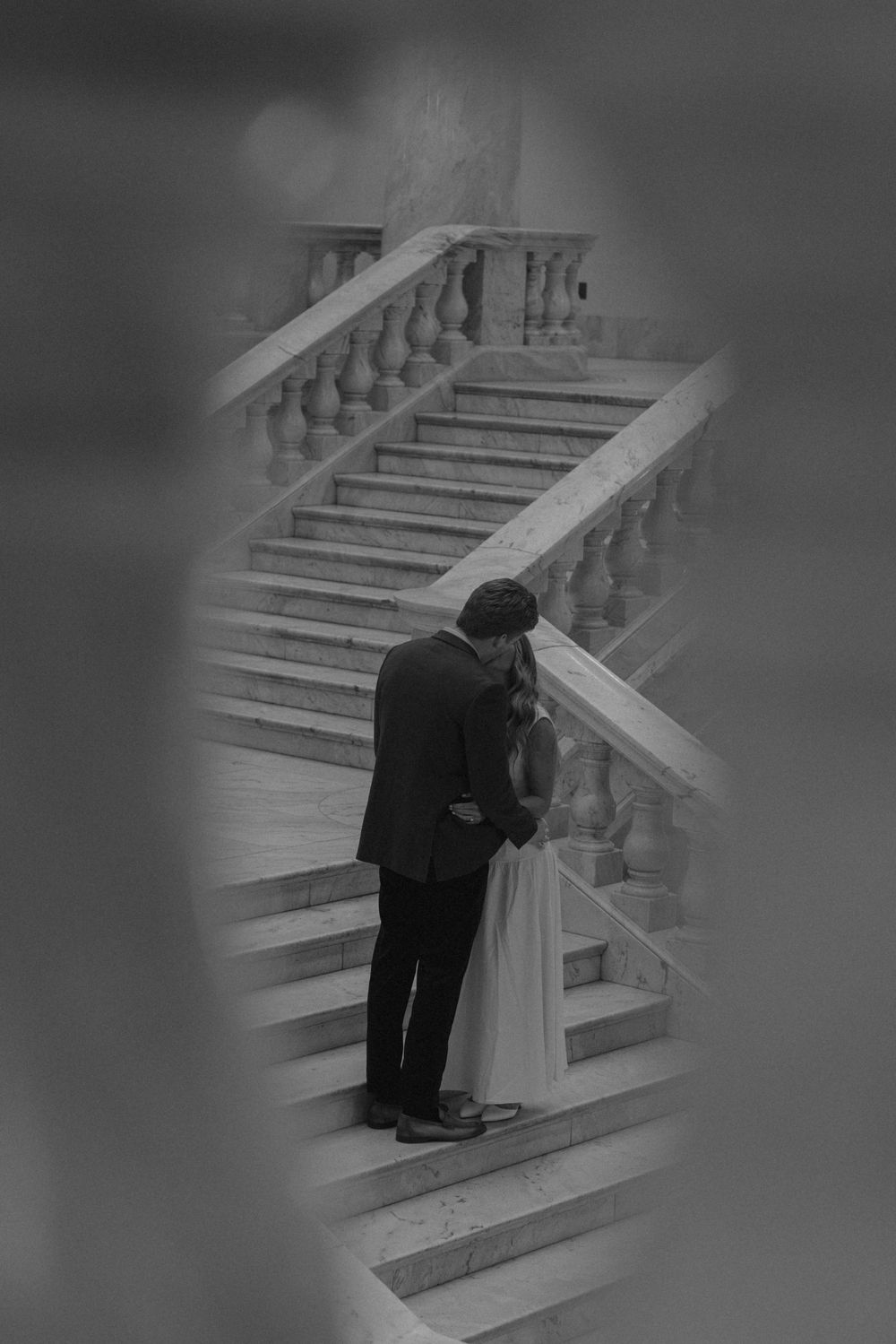 Black and white romantic photo of couple embracing on elegant marble staircase.
