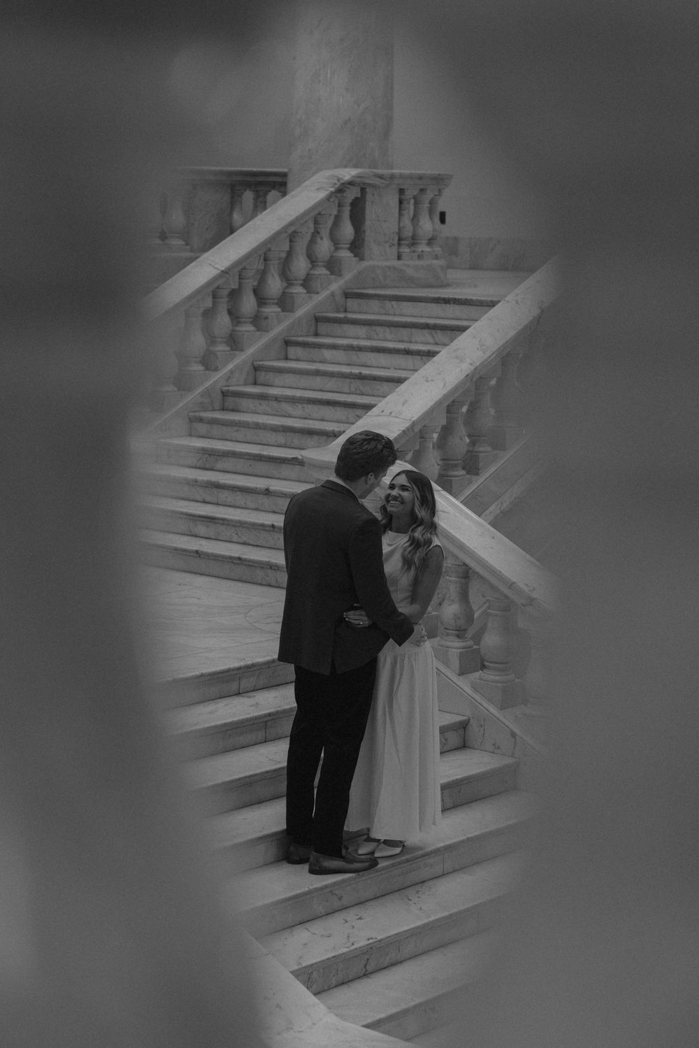 A couple shares a romantic moment on elegant marble stairs in a black and white photo.