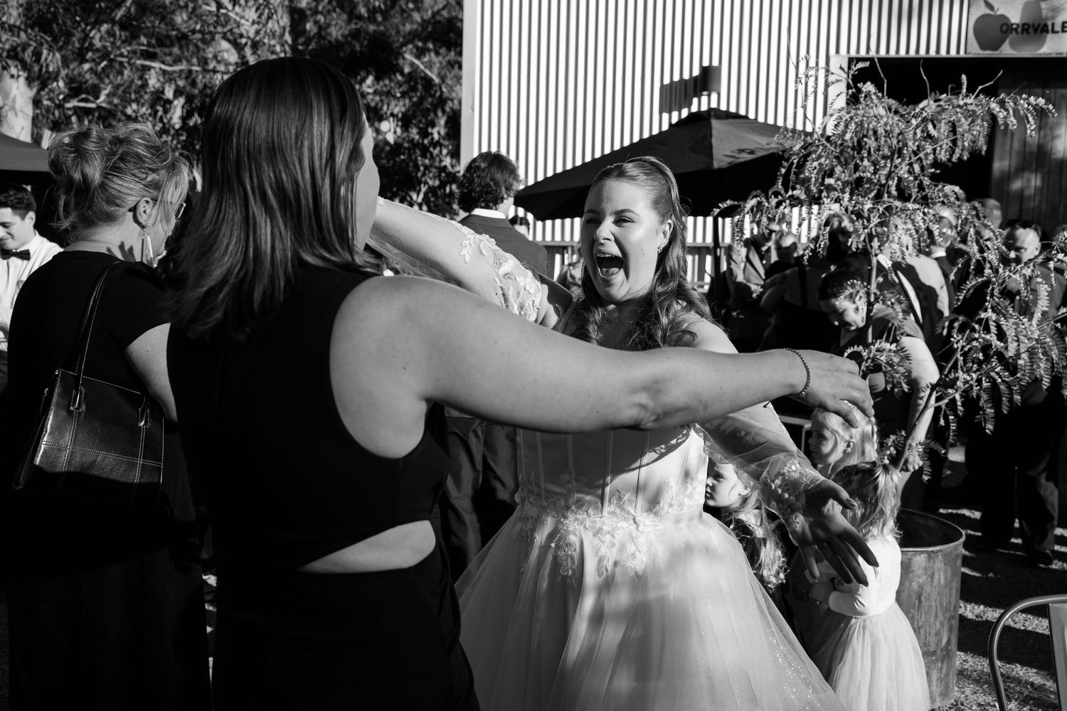 Black and white photo of women hugging and laughing at an outdoor wedding celebration.