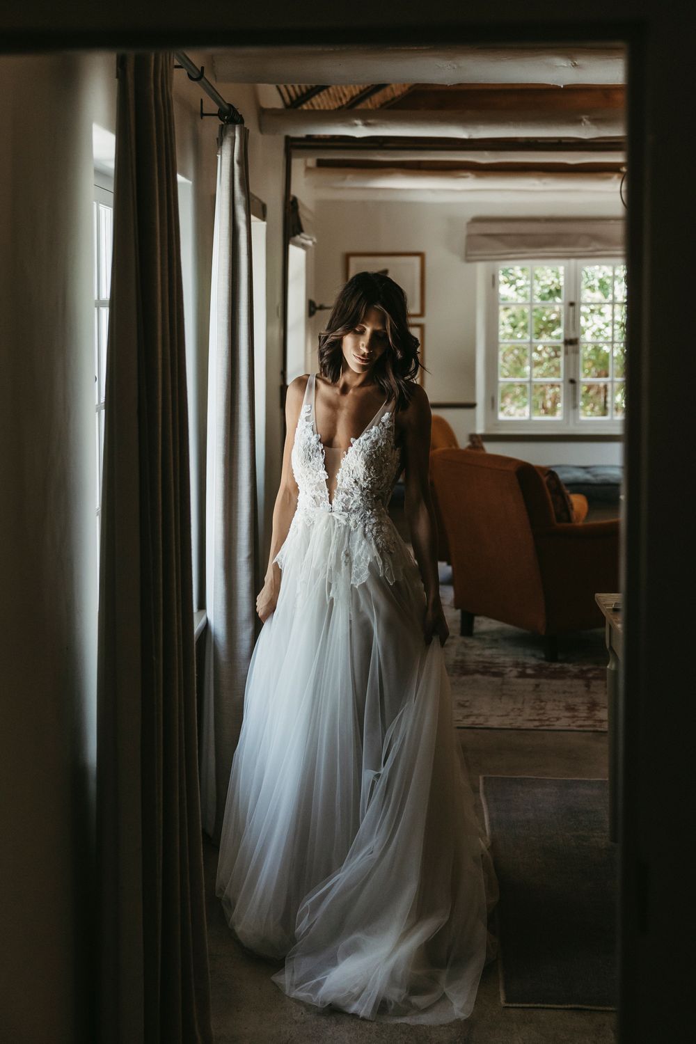 Dark-haired bride in a floral lace and tulle wedding gown standing in a rustic doorway.