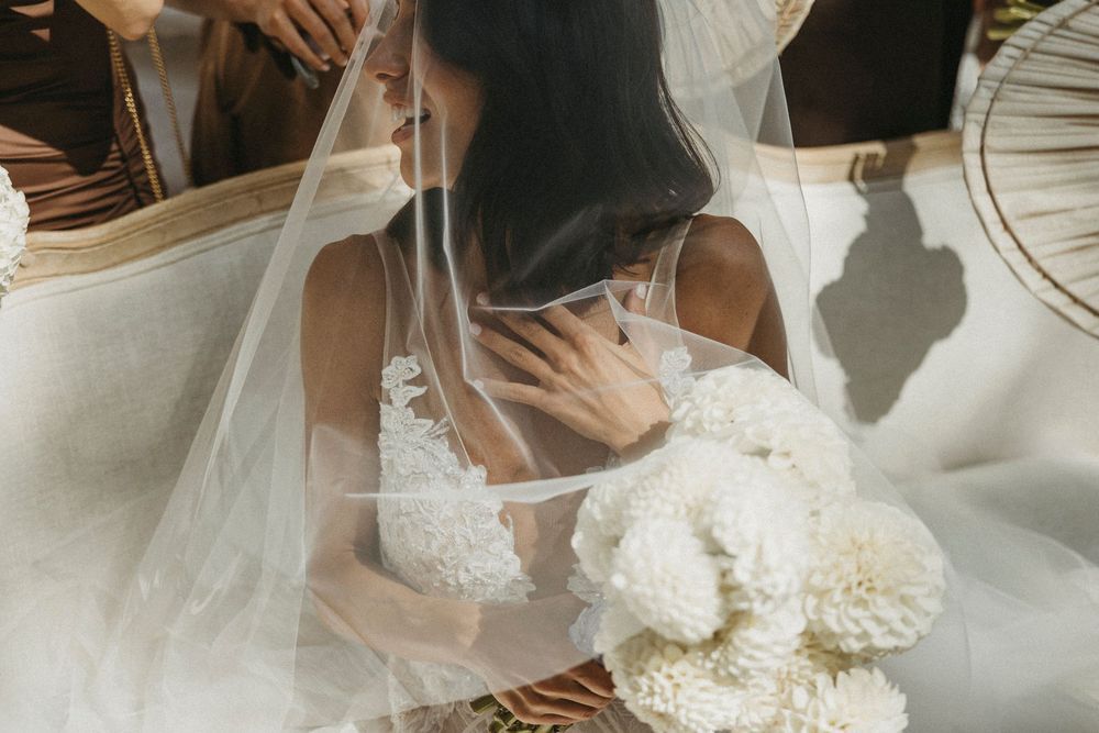 Close-up of bride in lace wedding dress holding white floral bouquet under sheer veil.