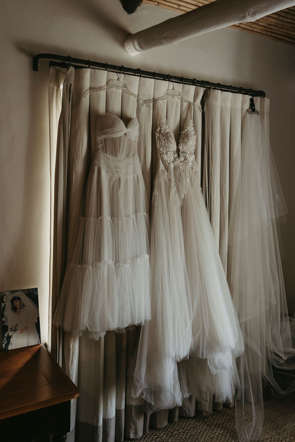 Two white tulle wedding gowns hanging on a rod in a warmly lit bridal suite.