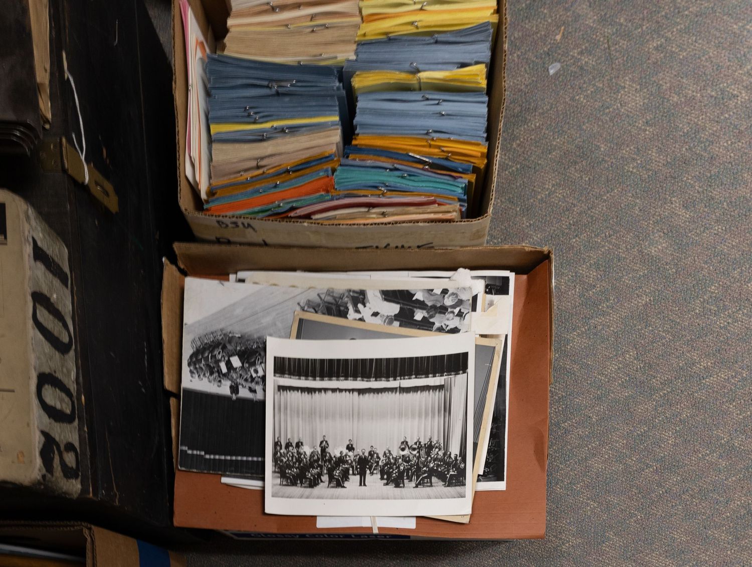Overhead view of two open boxes containing vintage black and white photographs and colorful file folders.