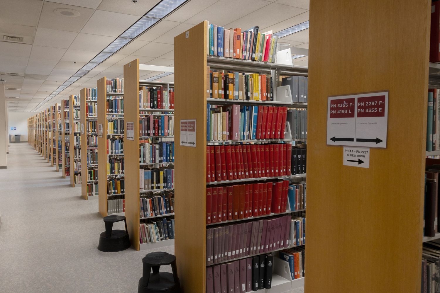 Long aisle of tall wooden library bookshelves filled with colorful reference books and red volumes.