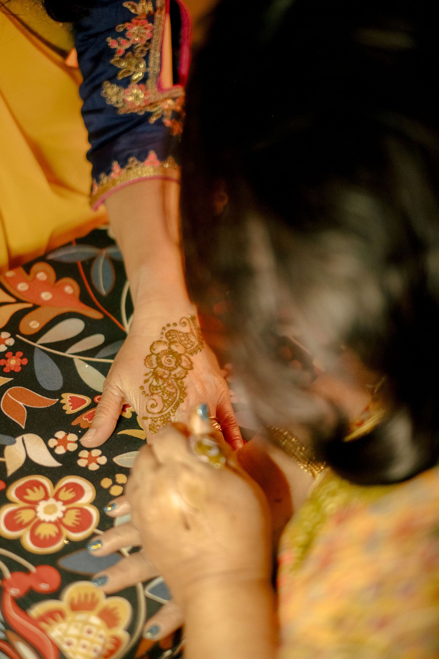 Woman applying intricate henna mehndi design on hand during traditional South Asian ceremony.