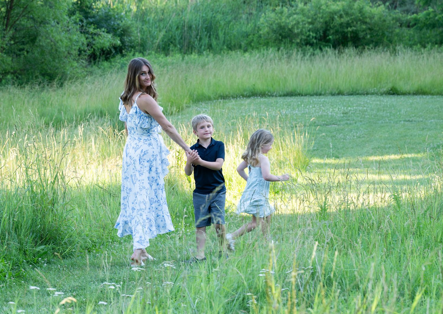 Children leading their mom down a grassy hill.