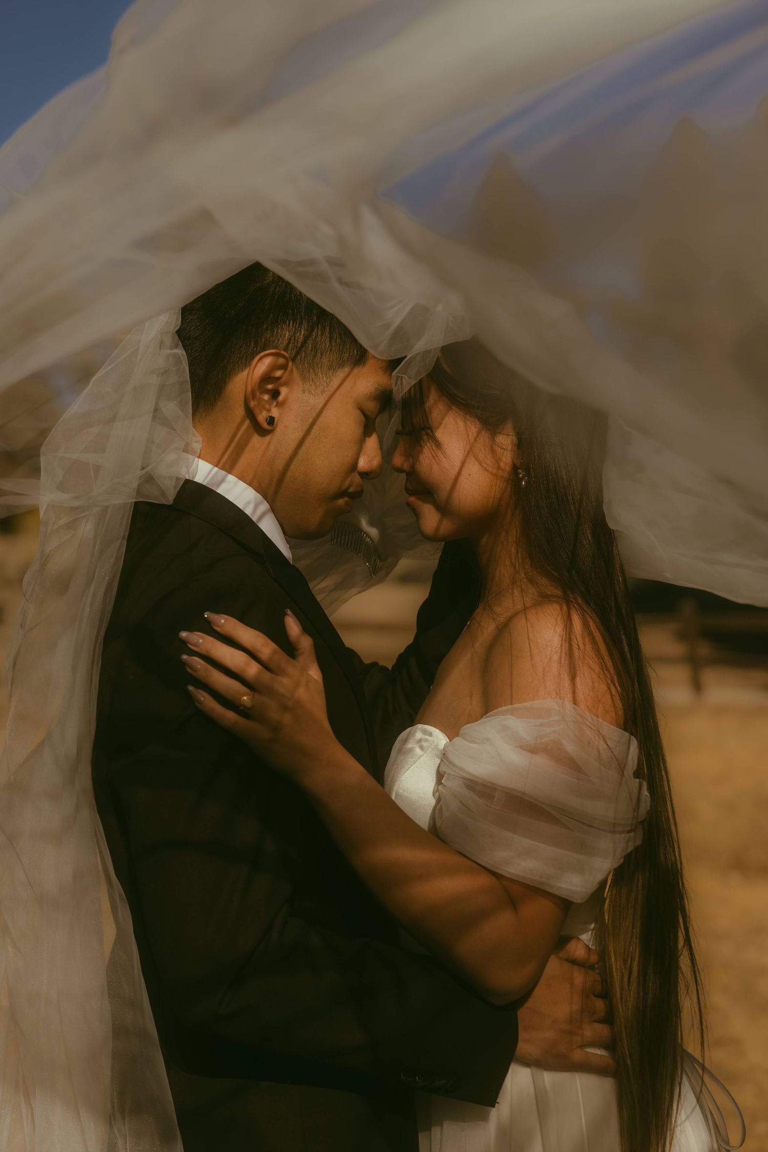 A couple shares an intimate moment under a flowing veil at their wedding ceremony in a golden field (Los Angeles wedding photographer)