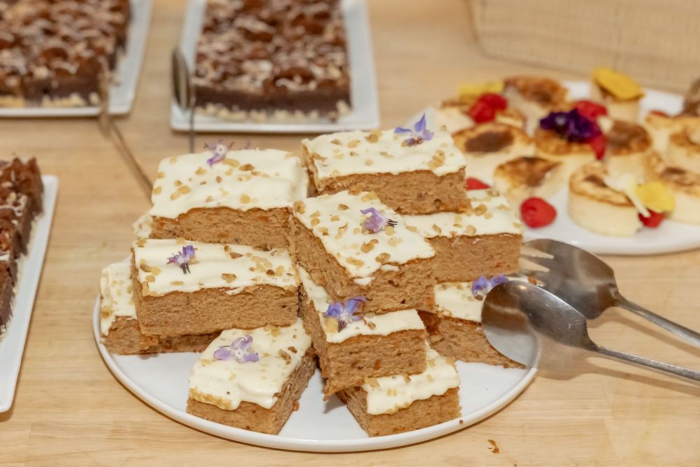 Frosted blondie bars topped with edible flowers on a white plate at a dessert table.