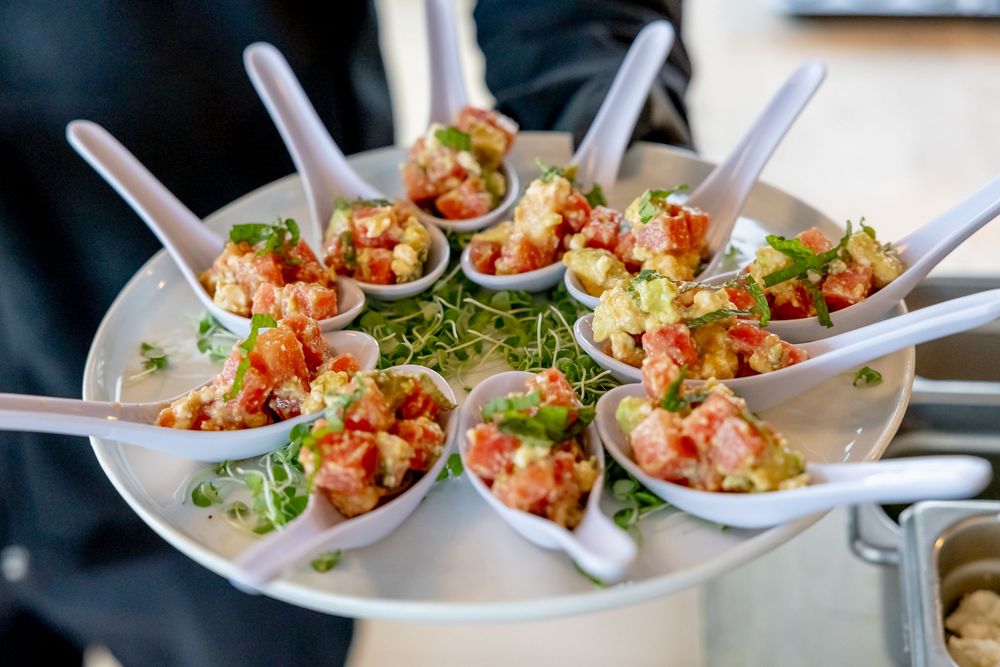 Elegant appetizer spoons with lobster salad and microgreens arranged on a round serving tray at a catered event.
