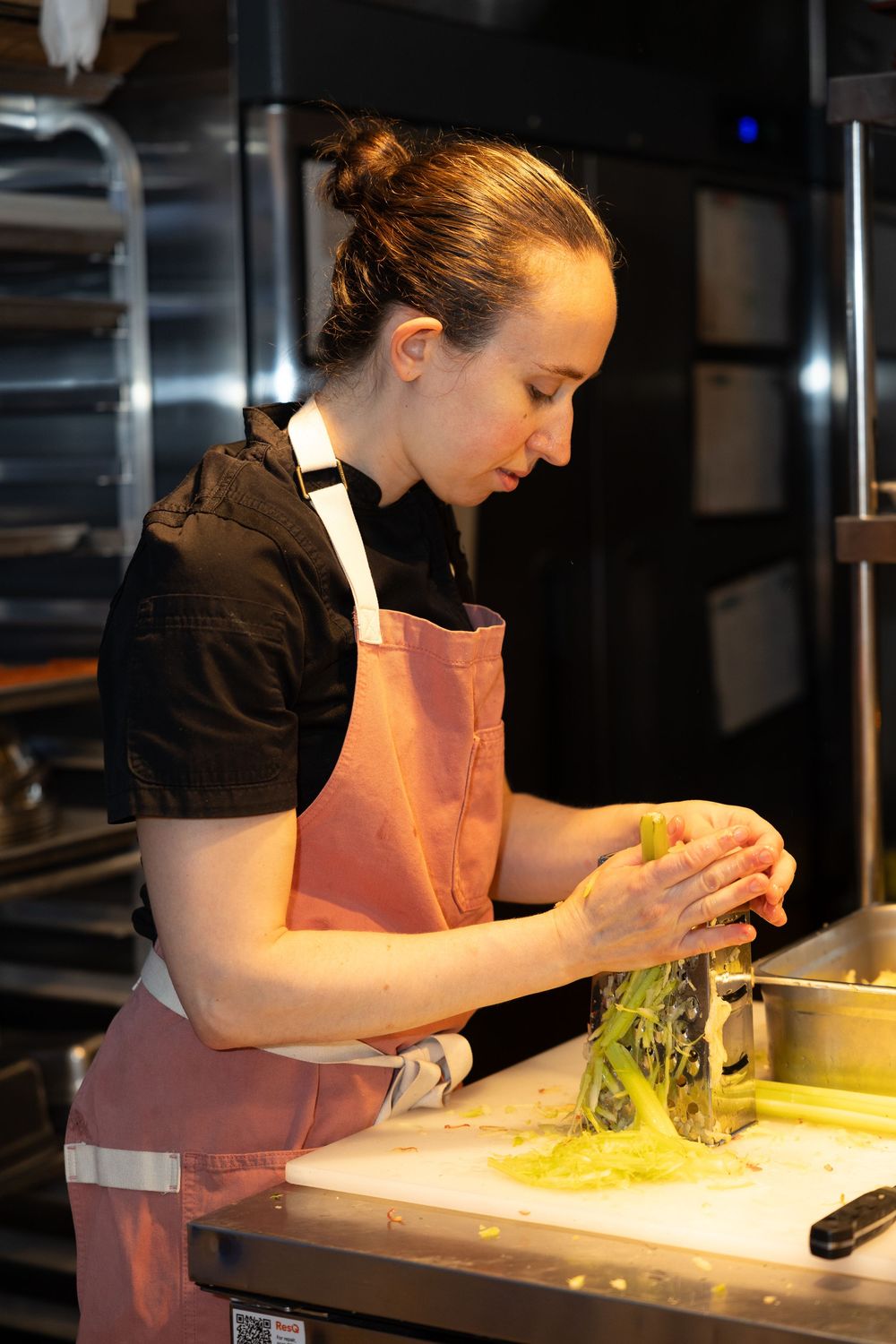 Female chef in pink apron preparing fresh green vegetables in a professional kitchen.