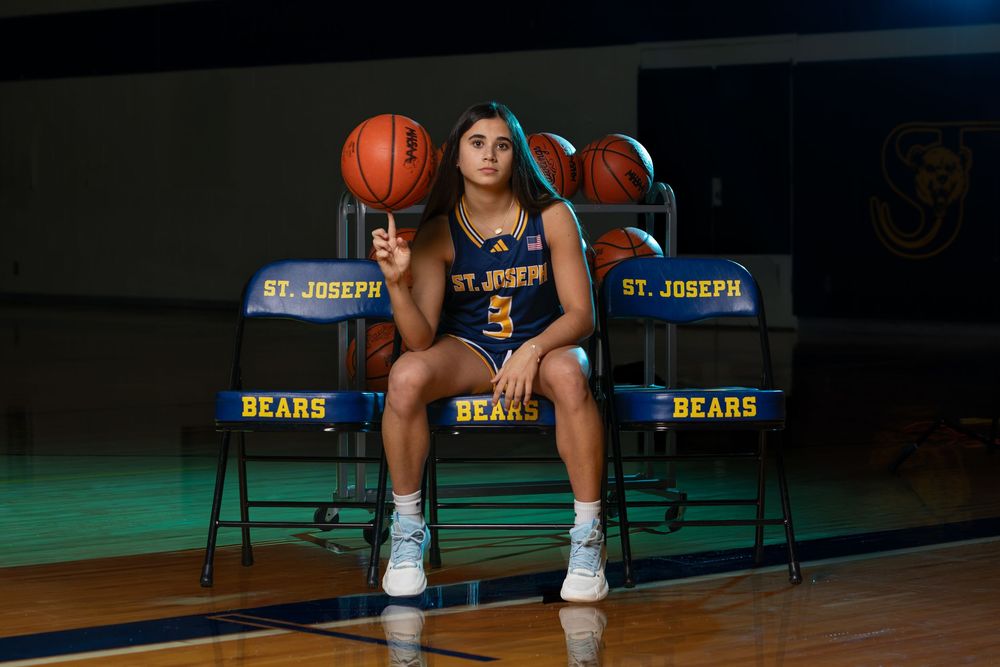 St. Joseph Bears female basketball player spinning ball on finger in blue jersey during team photo.