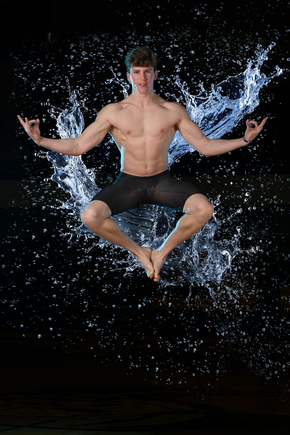 Athletic man in meditation pose levitating mid-air surrounded by dramatic water splashes on dark background.