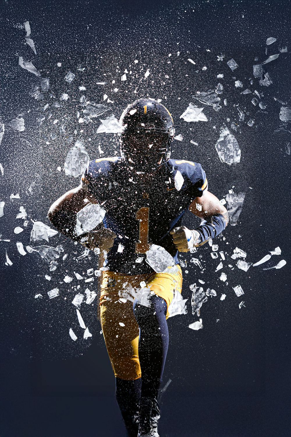 American football player in blue and gold uniform running through shattering glass explosion on dark background.