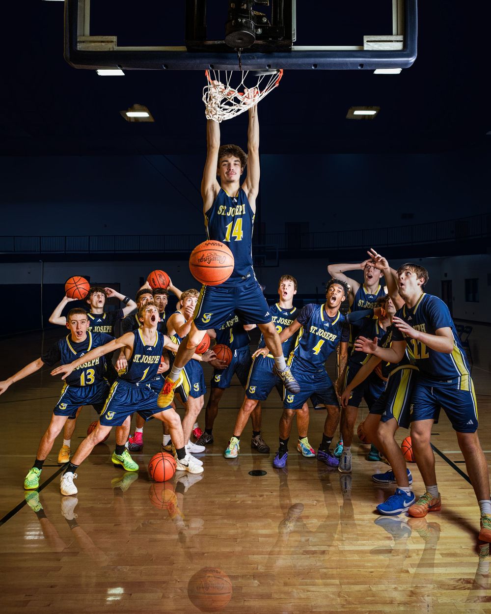 High school basketball team poses dramatically in gym, player #14 dunking while teammates react with excitement below.