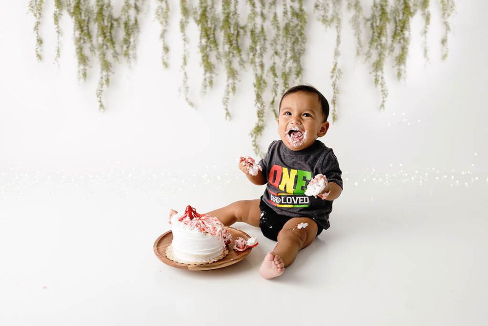 Happy smiling baby sits beside a smash cake during a first birthday photo session by professional Lake Elsinore photographer.